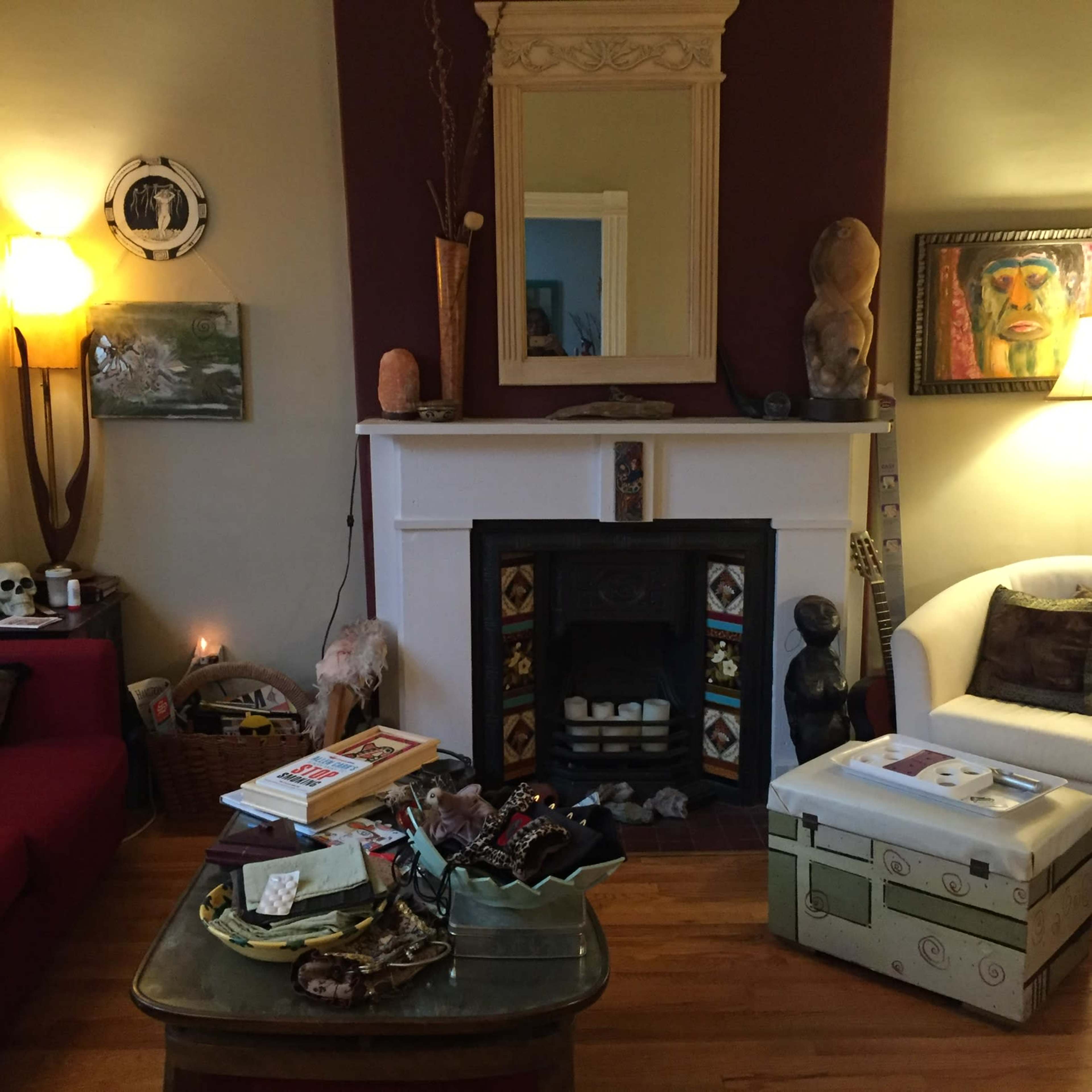 The living room features a fireplace with decorative elements, a coffee table cluttered with books and items, and a couch beside a lamp.