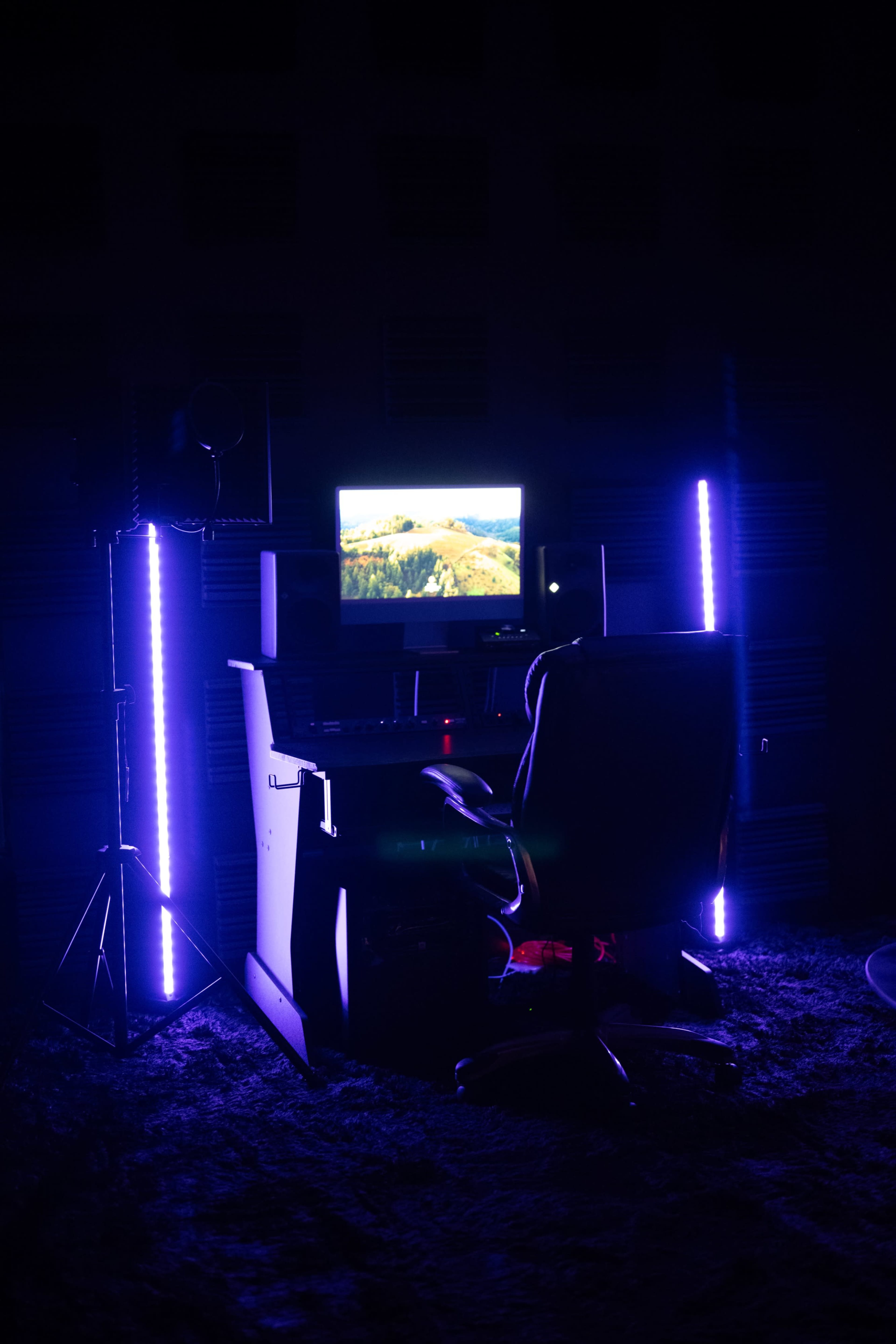 A desk with a computer monitor and a swivel chair is illuminated by blue LED lights in a dark room.