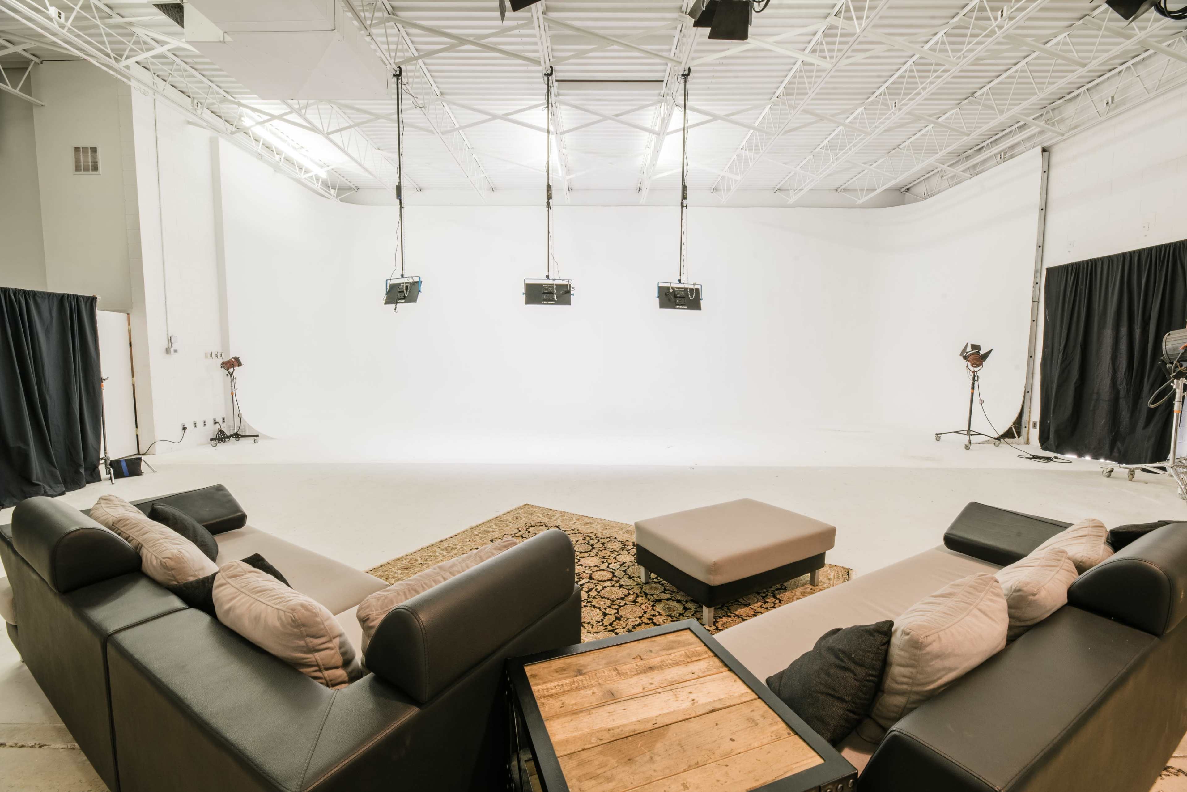 A modern studio with a spacious white backdrop, featuring a sectional sofa arrangement around a wooden coffee table.