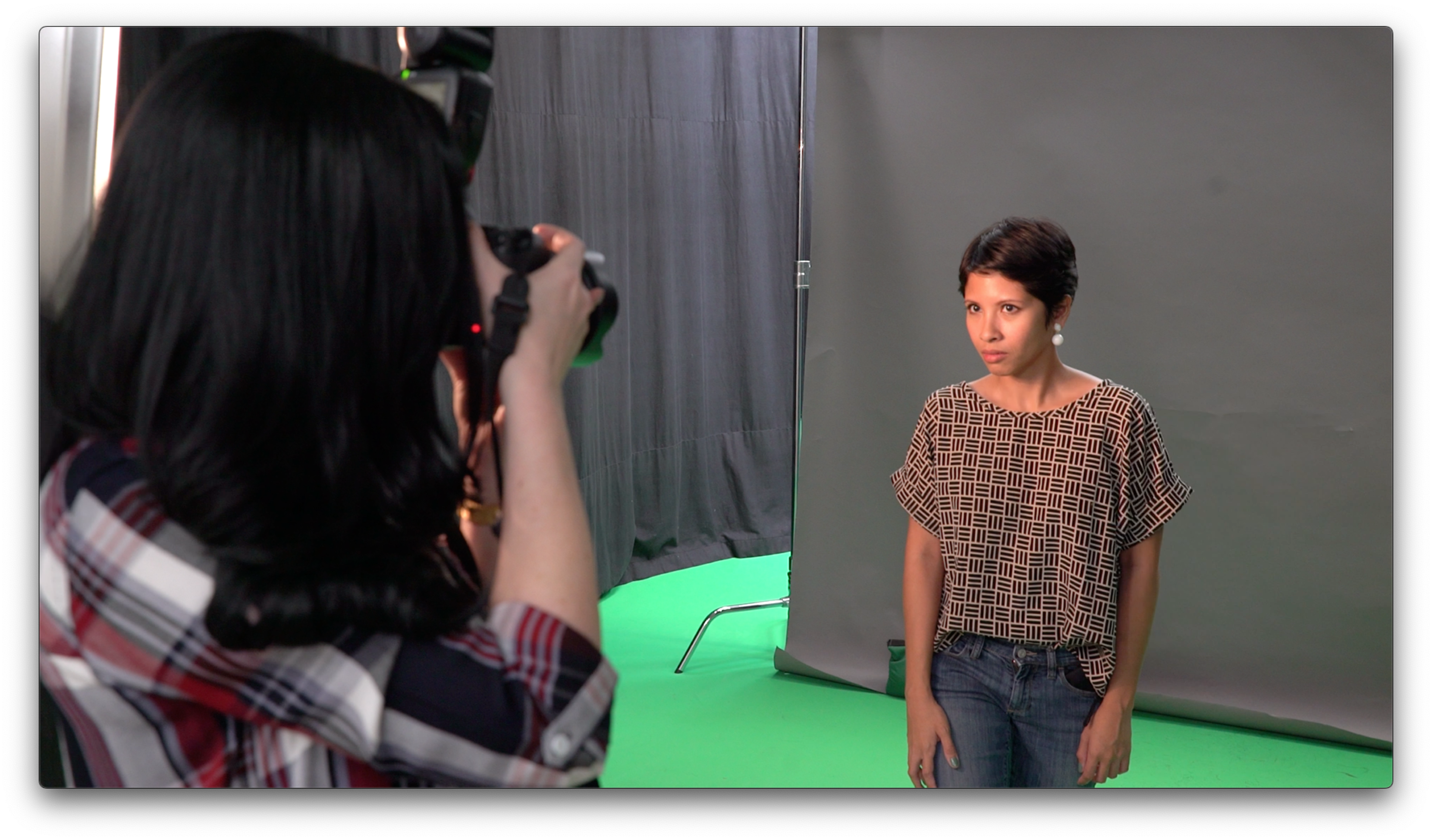 A woman is posing for a photo in front of a gray backdrop while a photographer captures the moment.