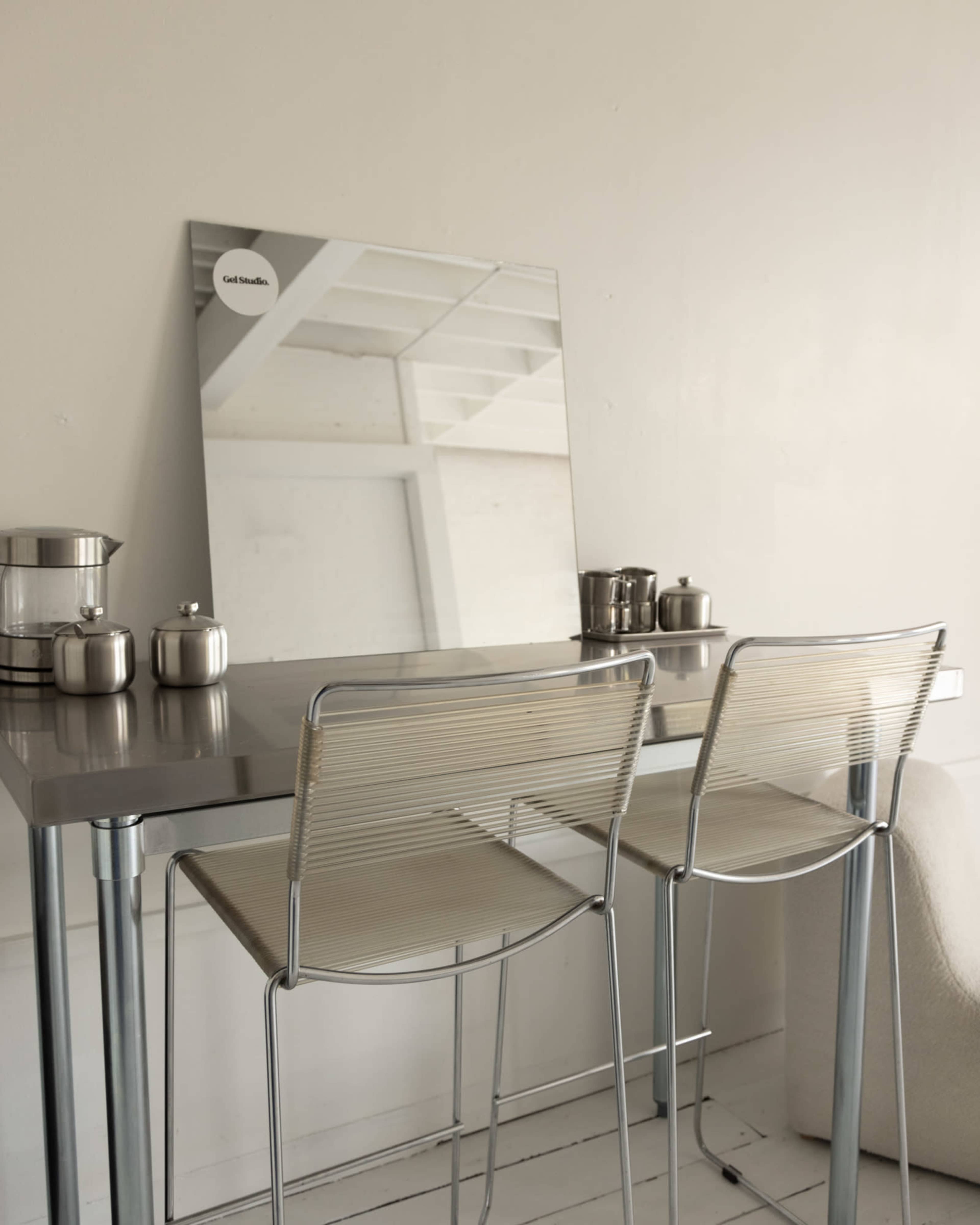 A modern dining area features a sleek table with two transparent chairs, a mirror on the wall, and metallic containers on the table.