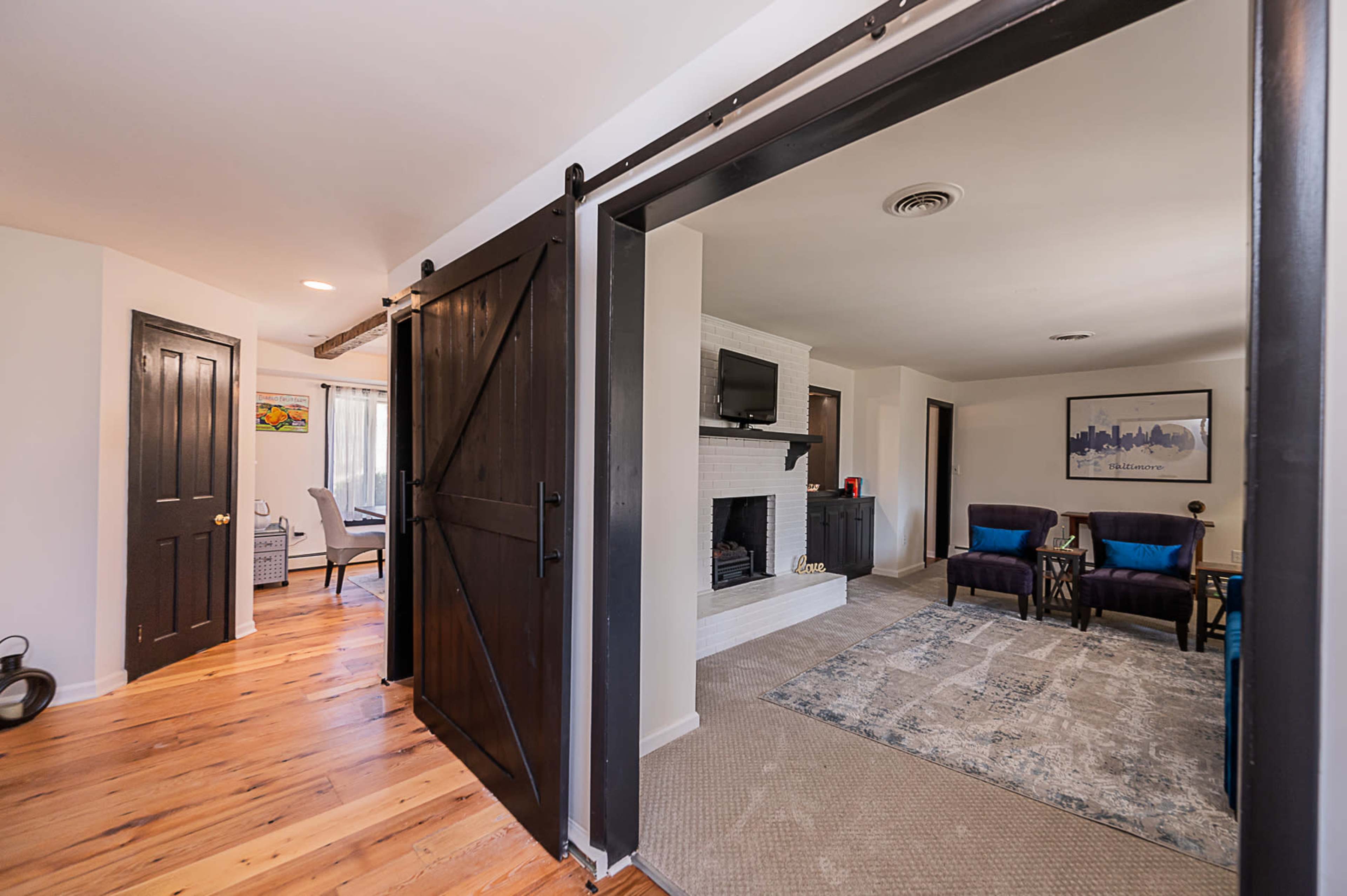 A spacious living area with a fireplace and seating arrangement, connected by a sliding barn door to an adjacent room.