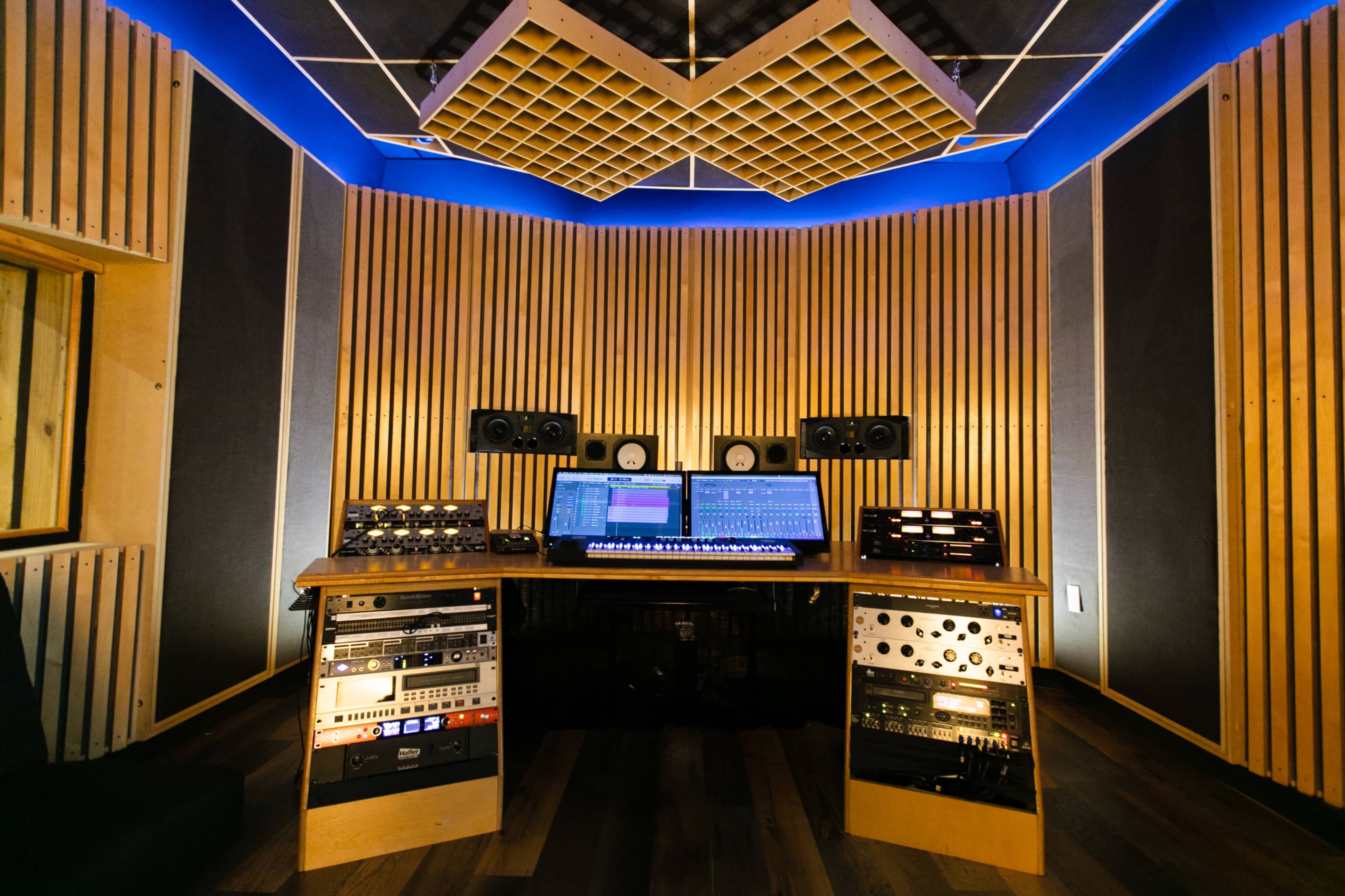 A professionally designed music recording studio featuring soundproof wooden walls, a control desk with an array of audio equipment, and speakers mounted on the wall.