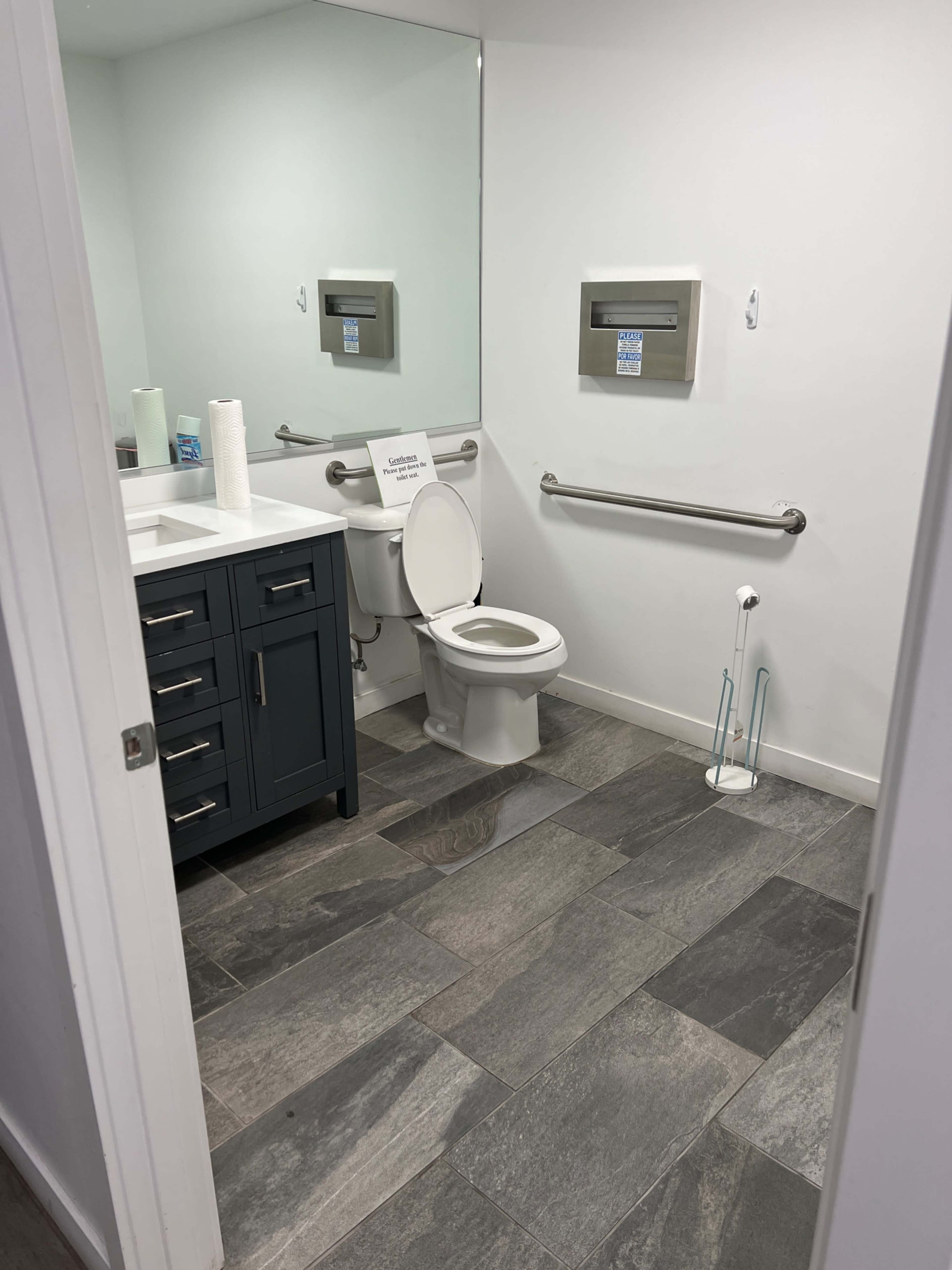 A clean restroom with a toilet, sink, mirror, and gray tiled flooring.