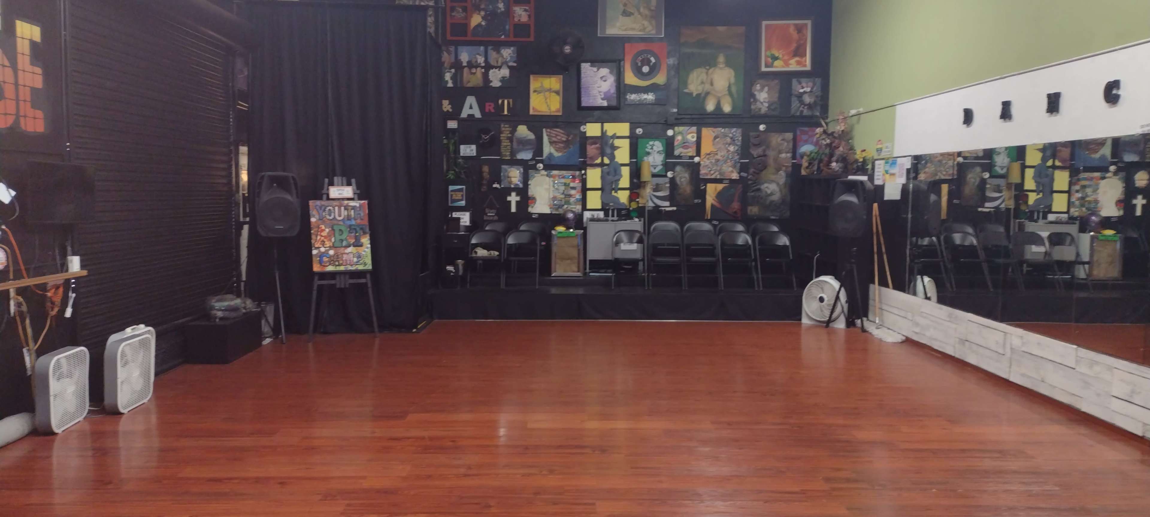 A dance studio with a polished wooden floor, black curtains, and walls decorated with various artworks and posters.