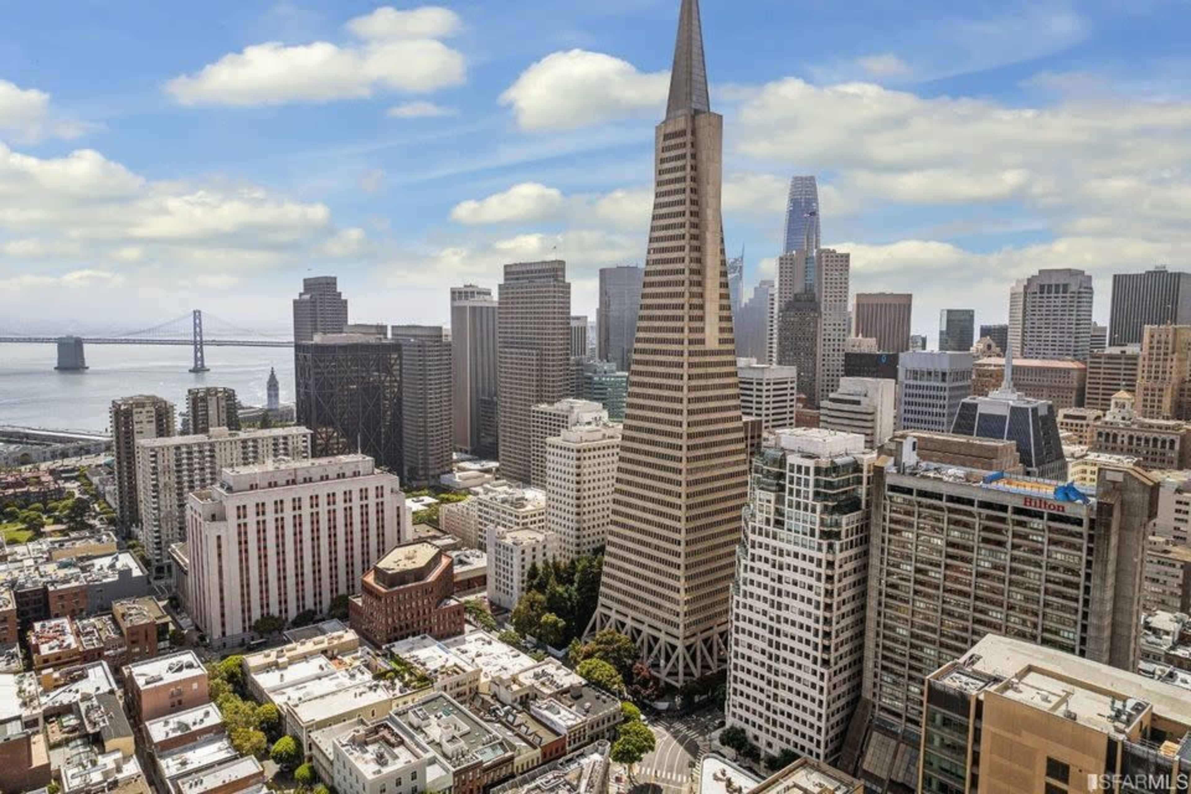 A panoramic view of San Francisco with the Transamerica Pyramid prominently in the foreground and the Bay Bridge visible in the background.