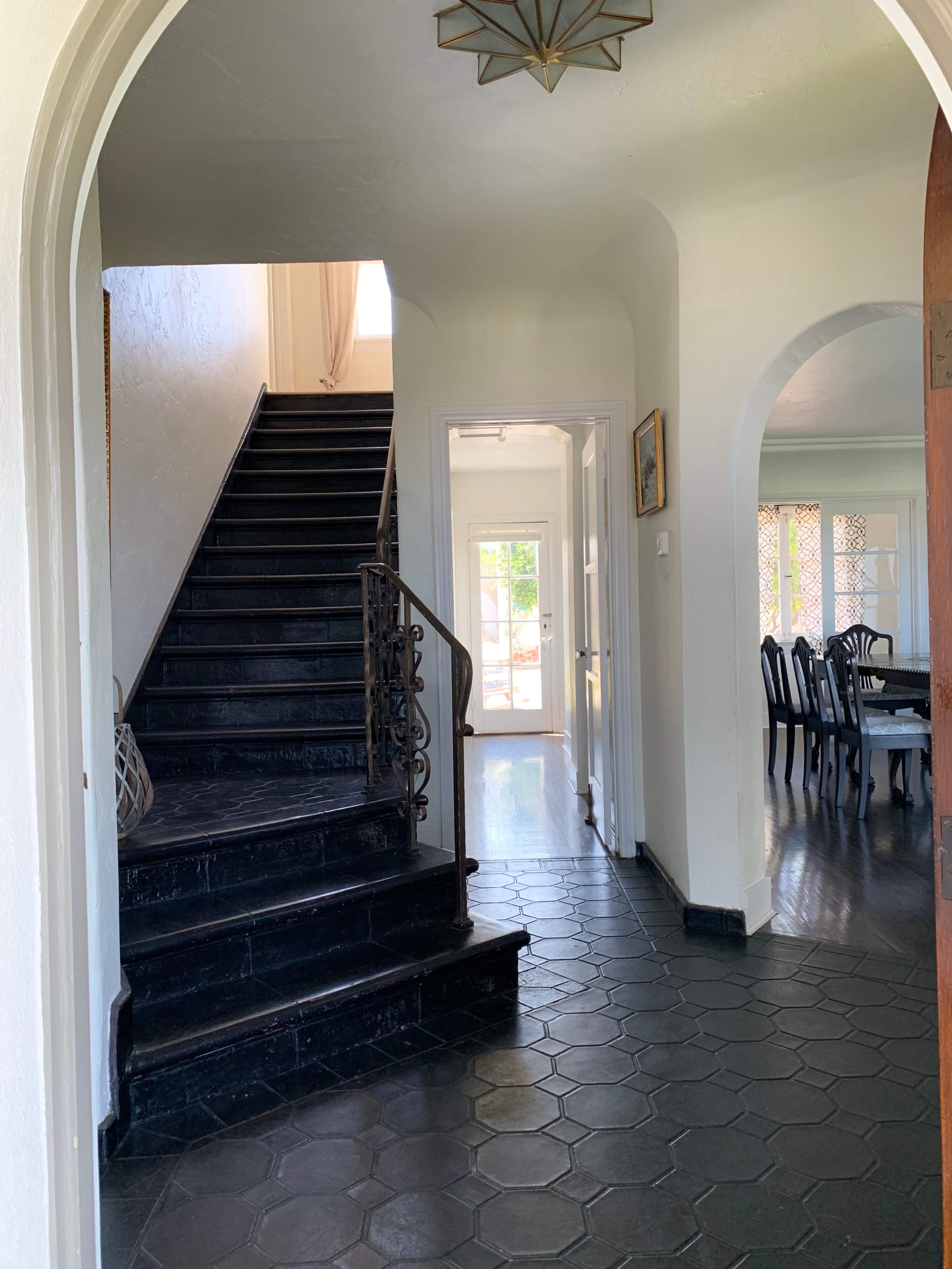 A hallway with a staircase on the left, leading to an upper level, and a dining area visible through an archway at the far end.