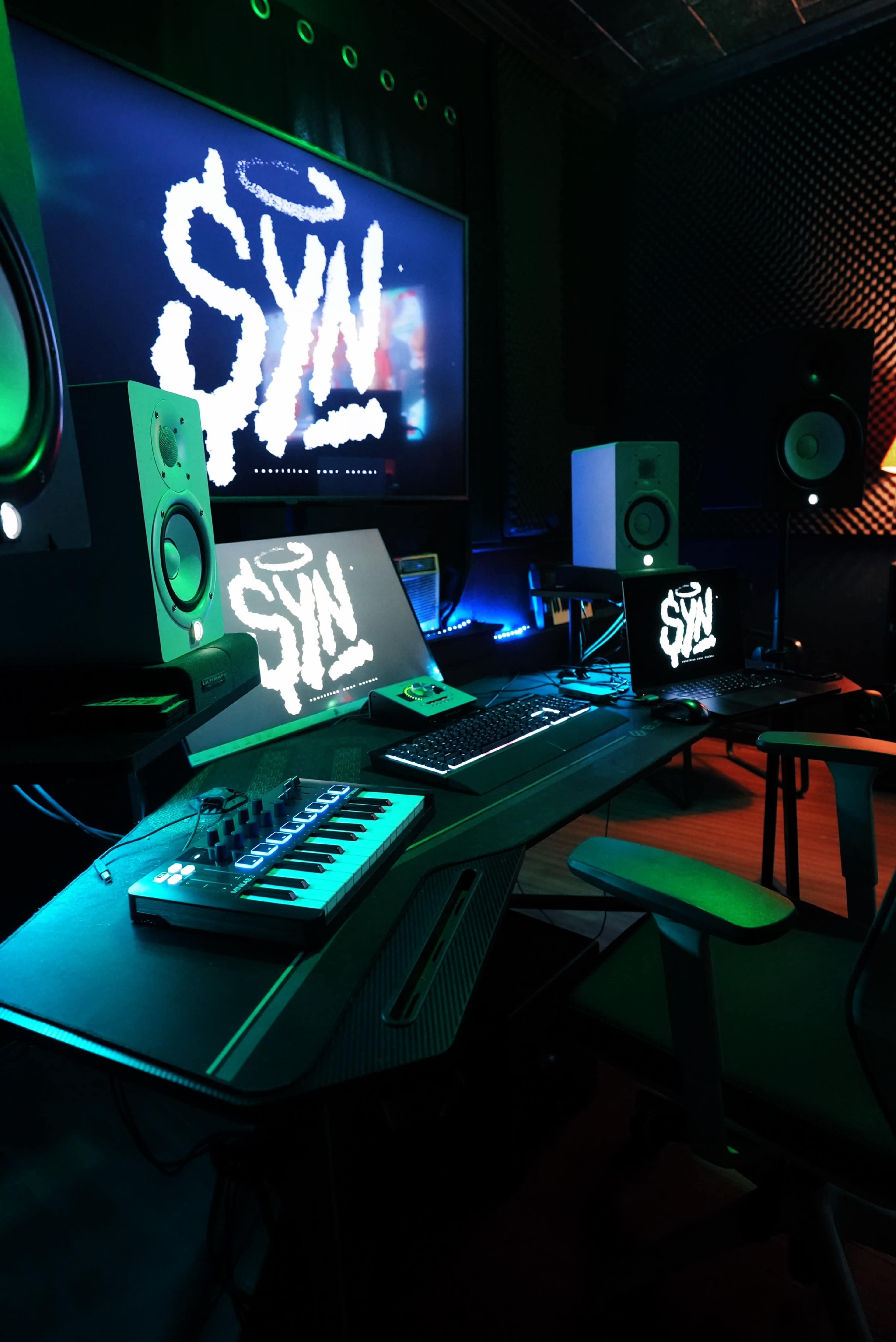 A music production studio features a sleek desk with a keyboard, monitor, and speakers, all illuminated by ambient lighting.