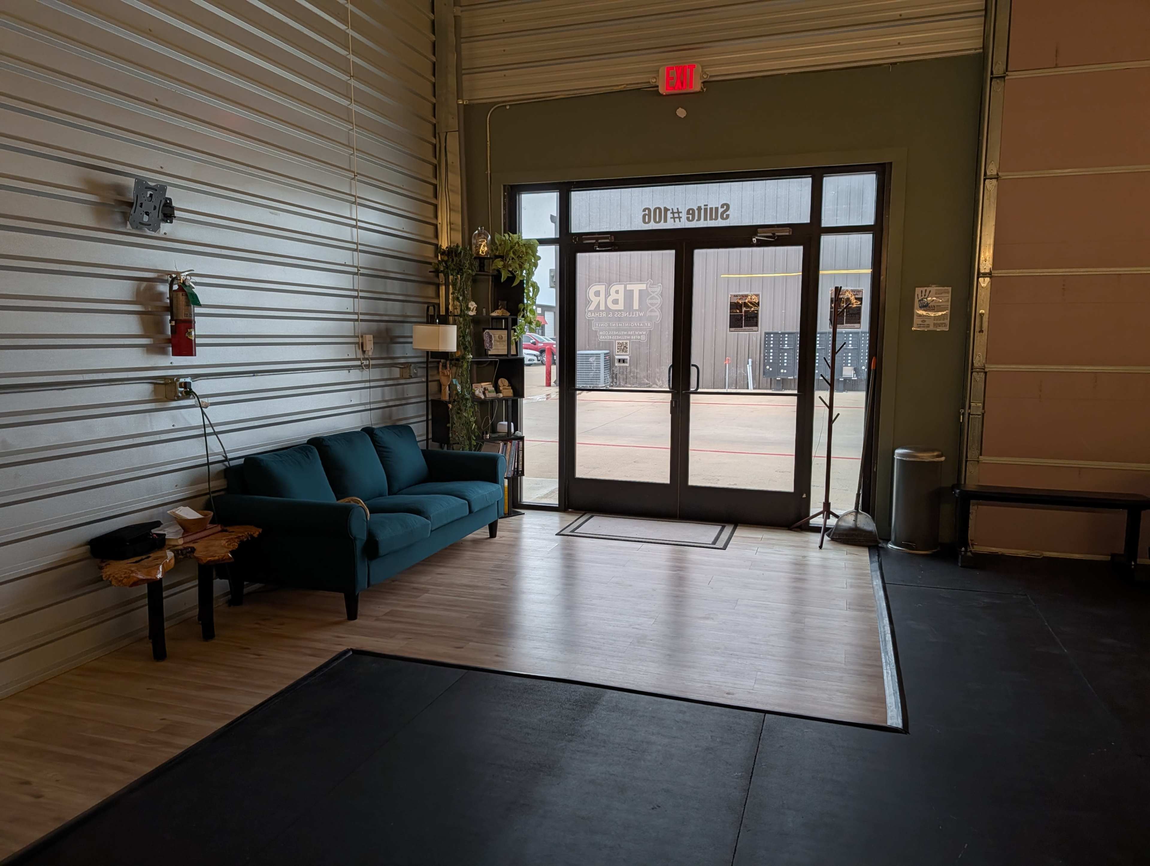 The image shows the interior of a commercial space featuring a green couch, a small table, and large glass doors leading outside.
