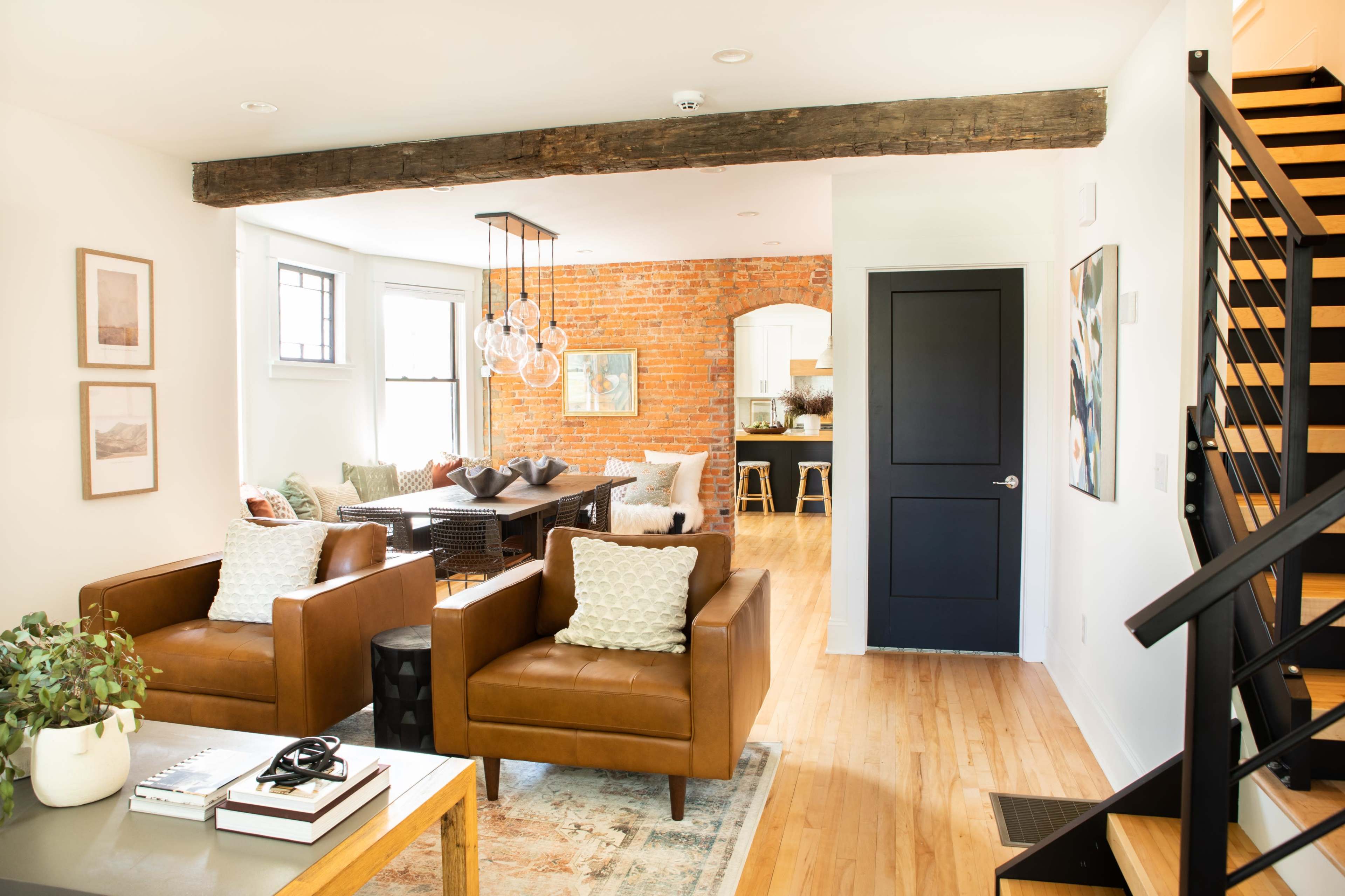 A modern living room with two brown leather chairs, a wooden beam across the ceiling, and a view of a dining area with a brick wall in the background.