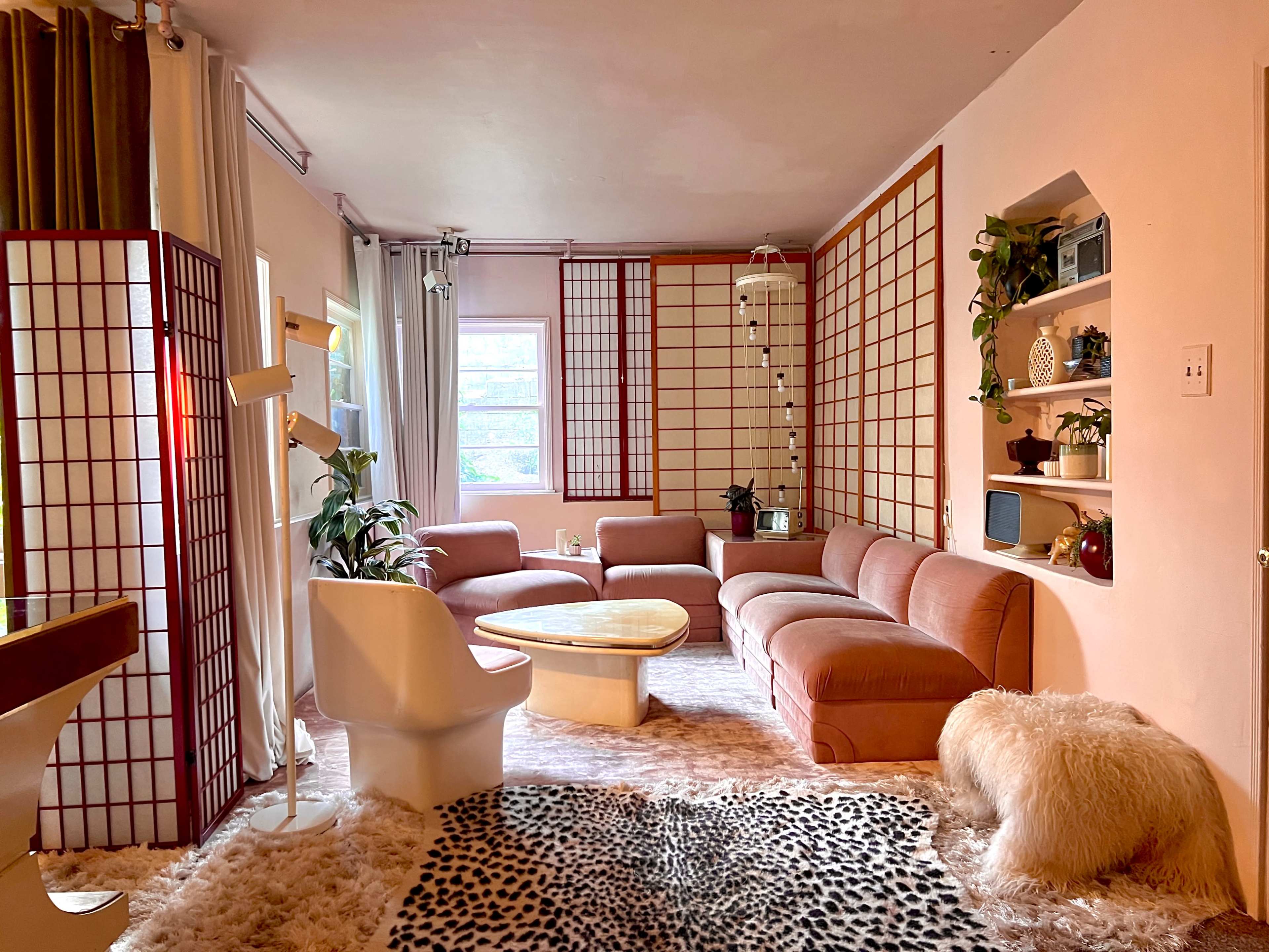 A cozy living room with a large curved pink sofa, a wooden coffee table, and decorative room dividers.