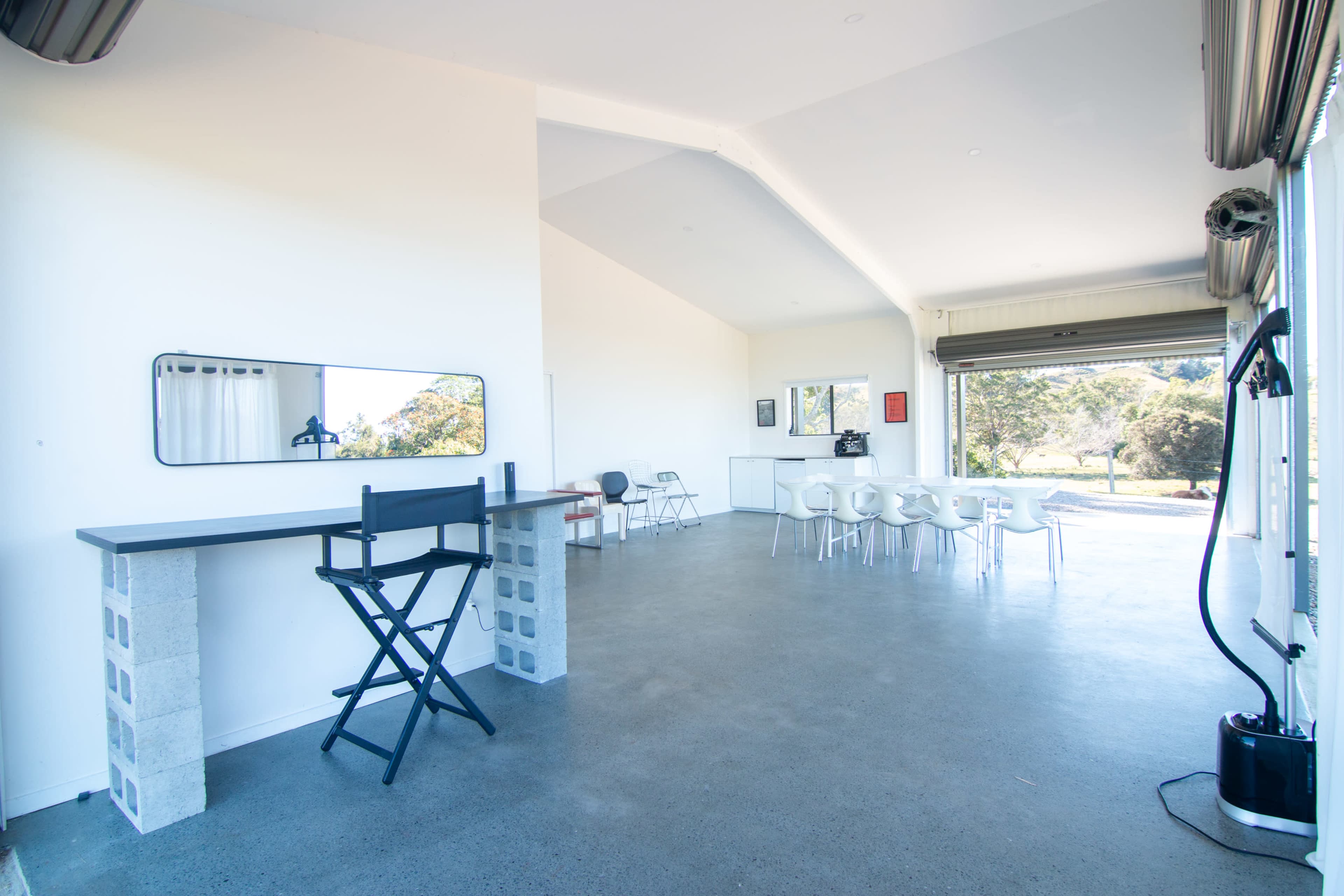 The image shows a spacious modern interior with a large open area featuring a bar-style seating space, concrete flooring, and a dining table surrounded by white chairs.