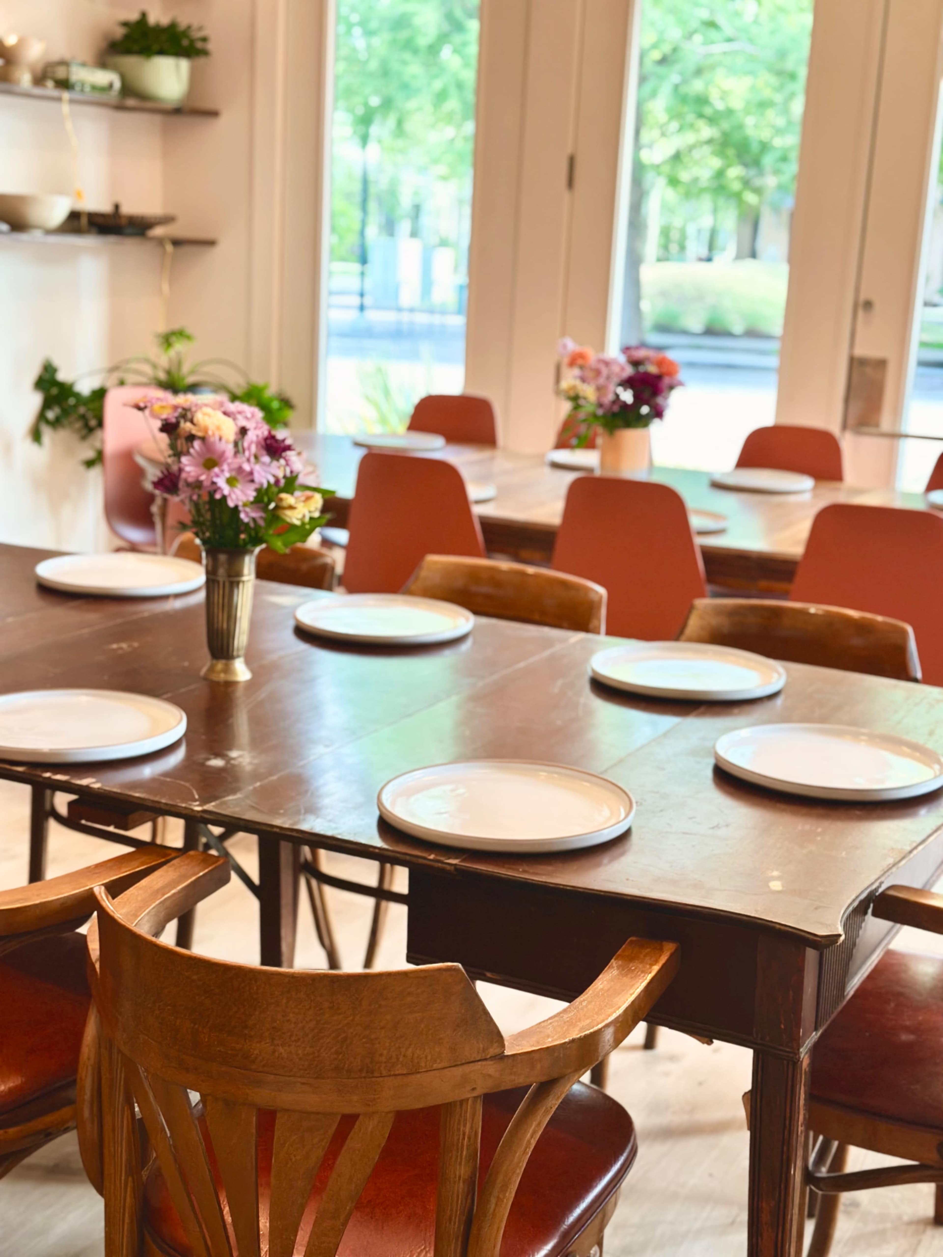 A dining area features several wooden tables set with plates and decorated with flower arrangements in vases.