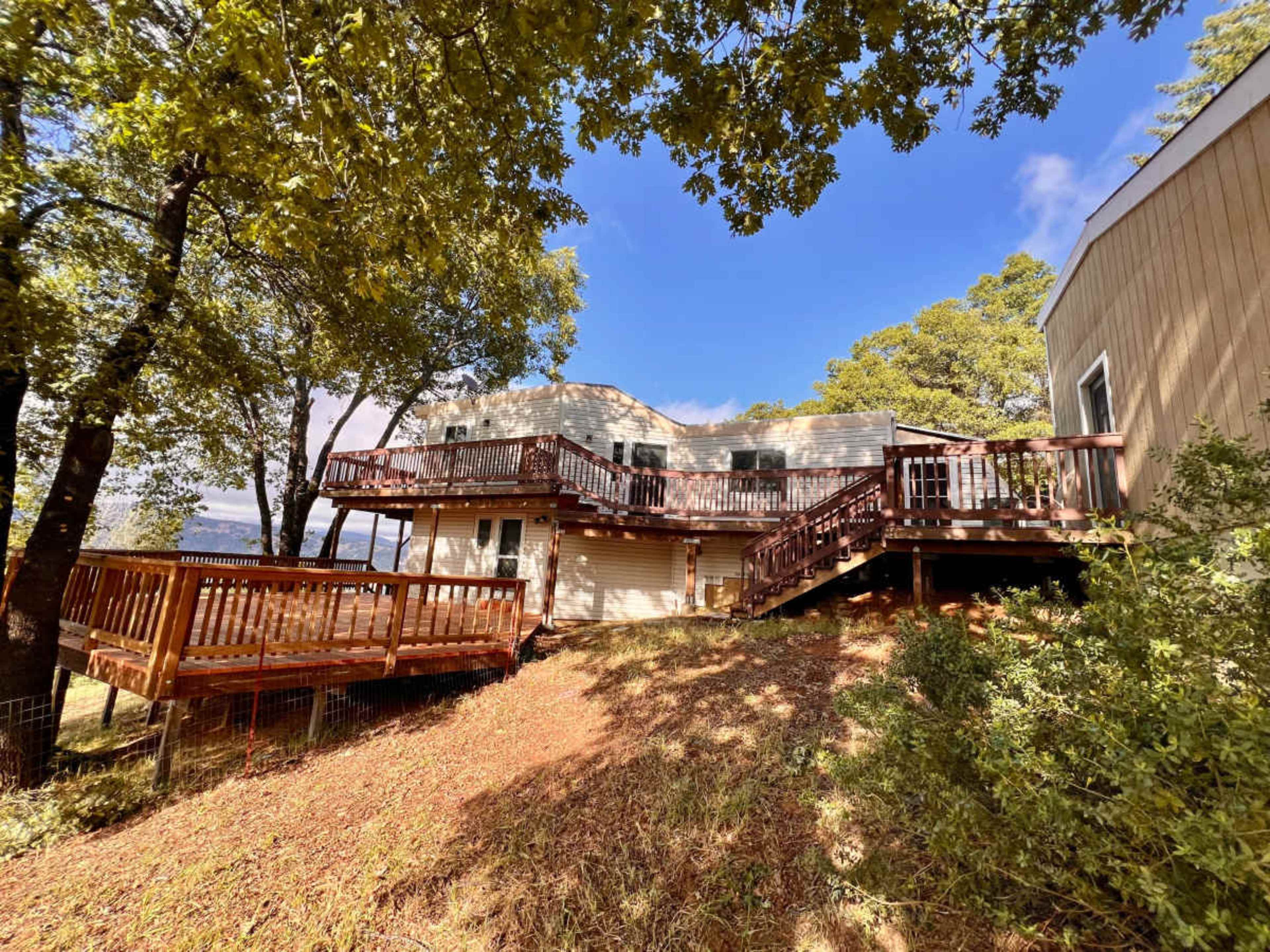 A multi-level house with wooden decks is surrounded by trees and situated on a hillside.