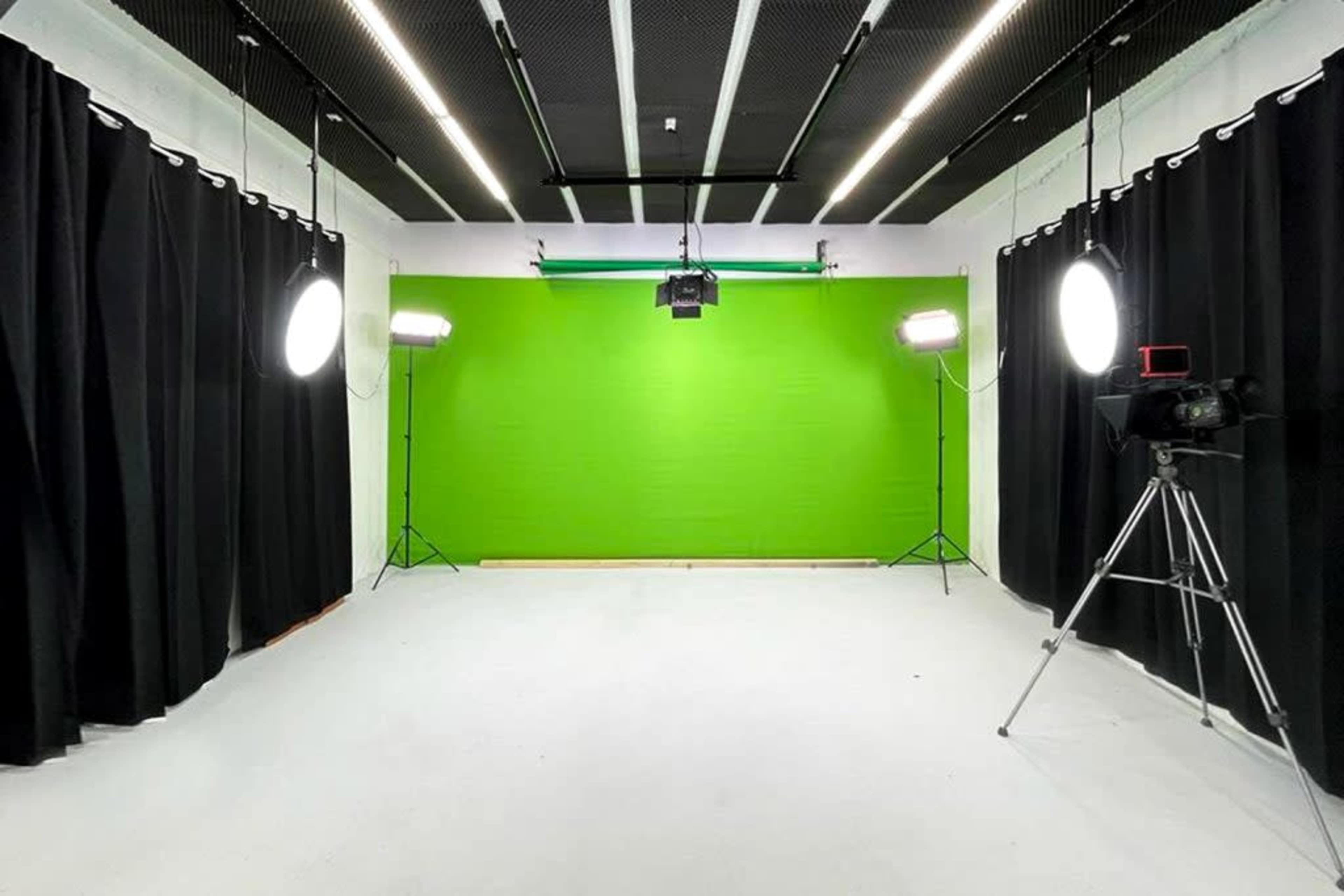 A brightly lit studio with a green backdrop, black curtains, and various lighting equipment.
