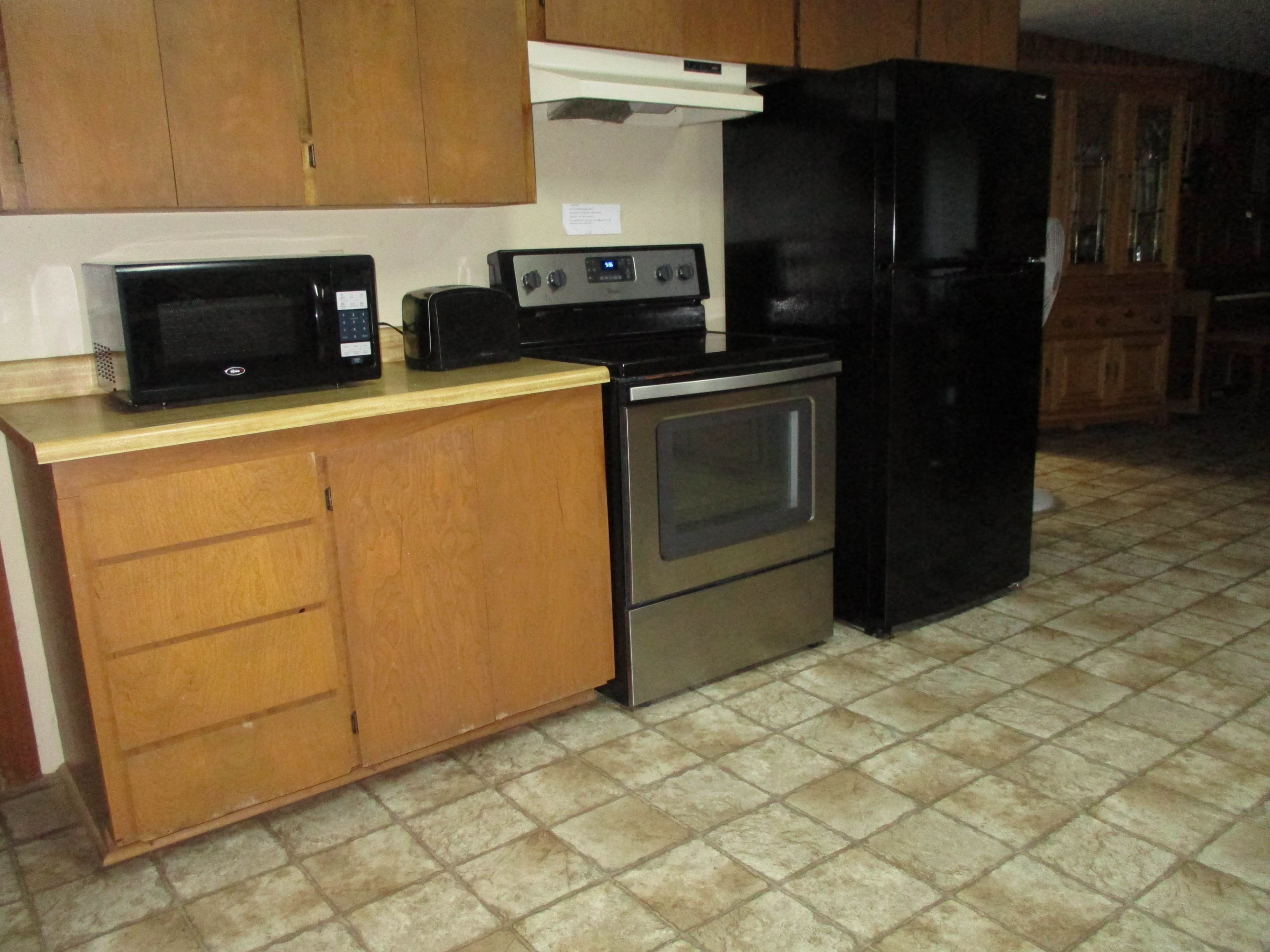 A kitchen with wooden cabinets, a microwave, a toaster, a stove, and a black refrigerator, all positioned on a tiled floor.