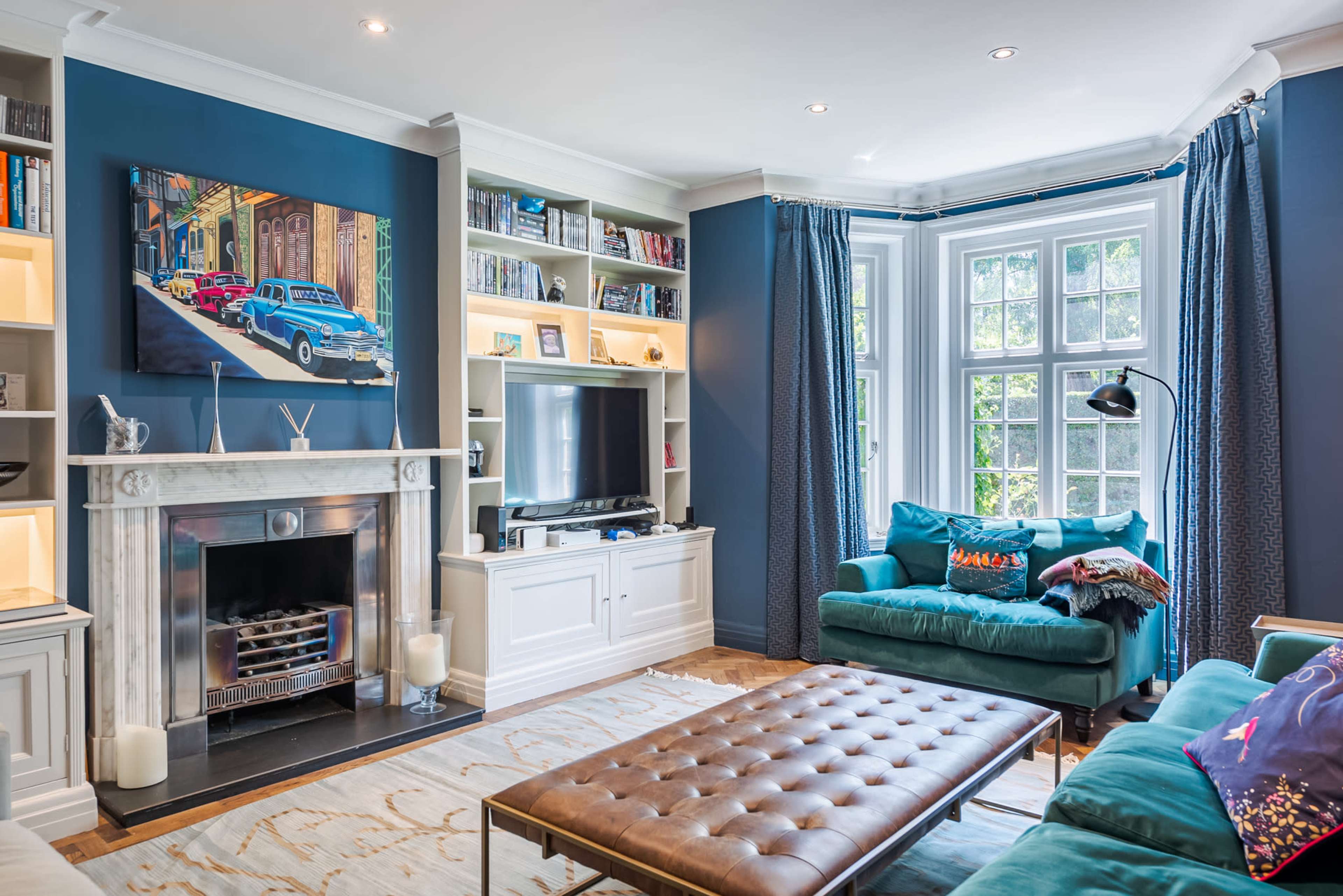 The living room features a blue accent wall, a marble fireplace, a television in a built-in unit, and a combination of comfortable seating options.
