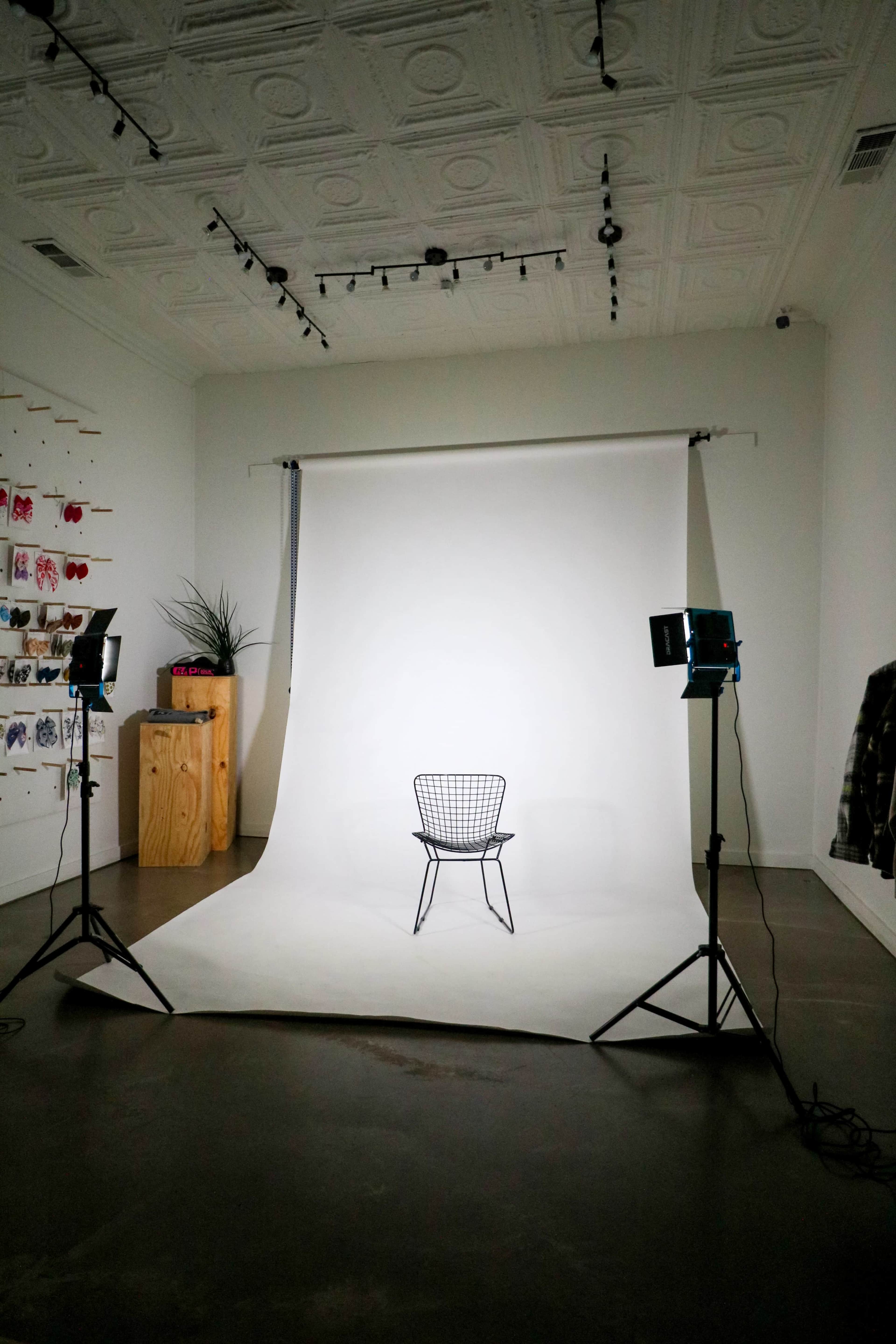 A minimalist photo studio setup features a single chair on a white backdrop, illuminated by two studio lights.