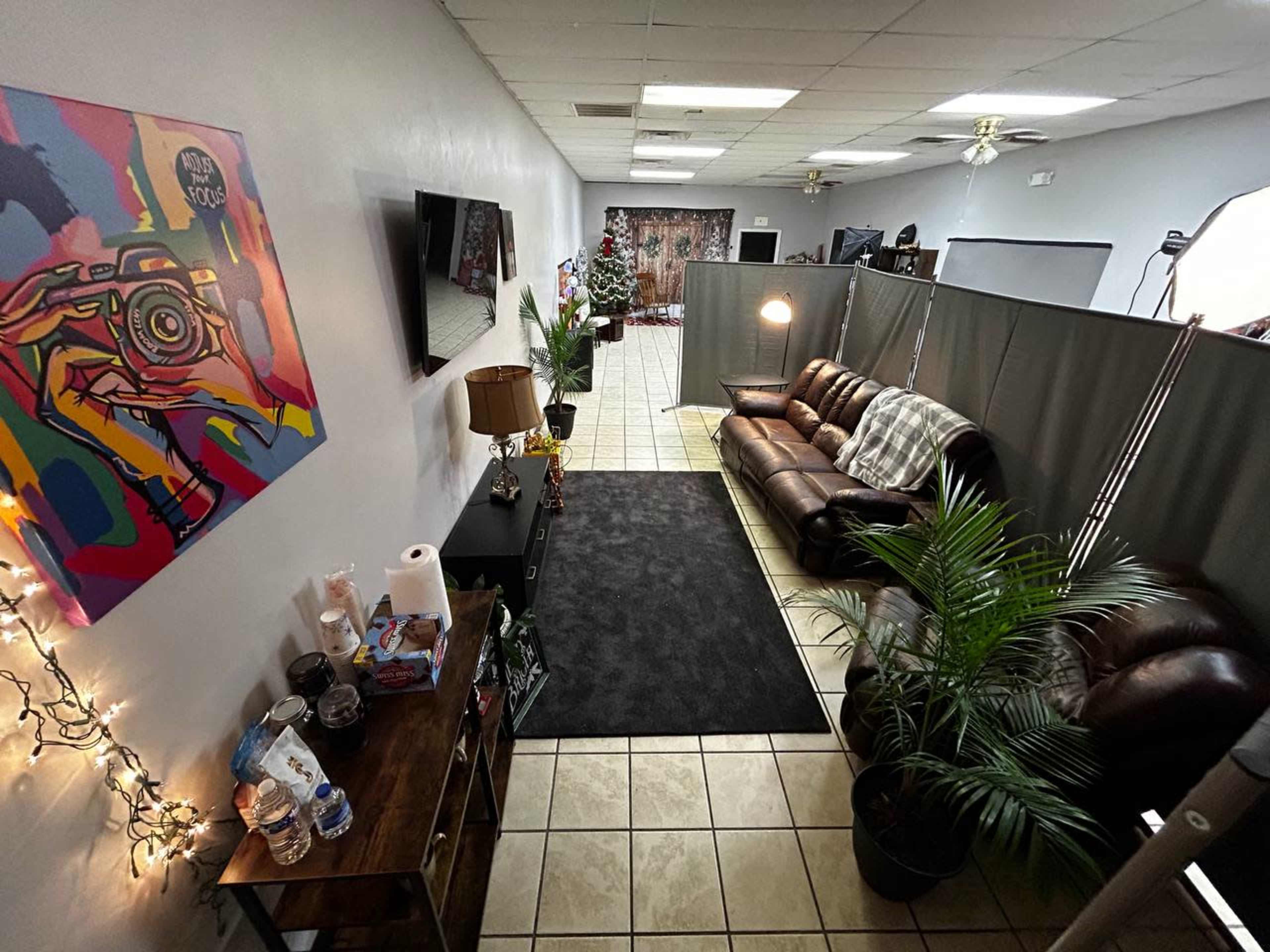 A spacious interior with a brown leather sofa, a coffee table, and decorative plants, along with colorful artwork on the wall and divider panels creating separate areas.