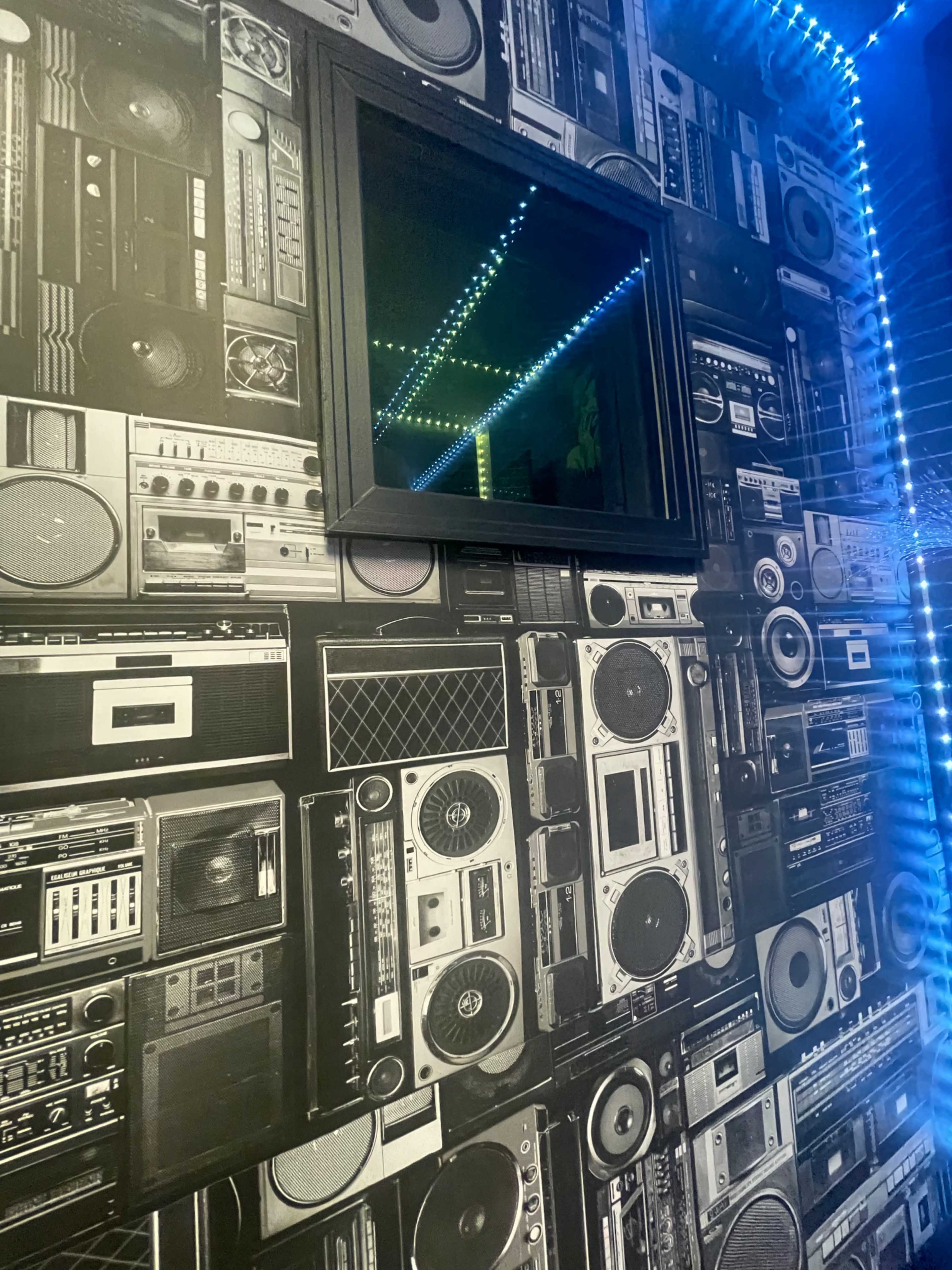 A wall decorated with a retro boombox-patterned wallpaper and a black-framed mirror.