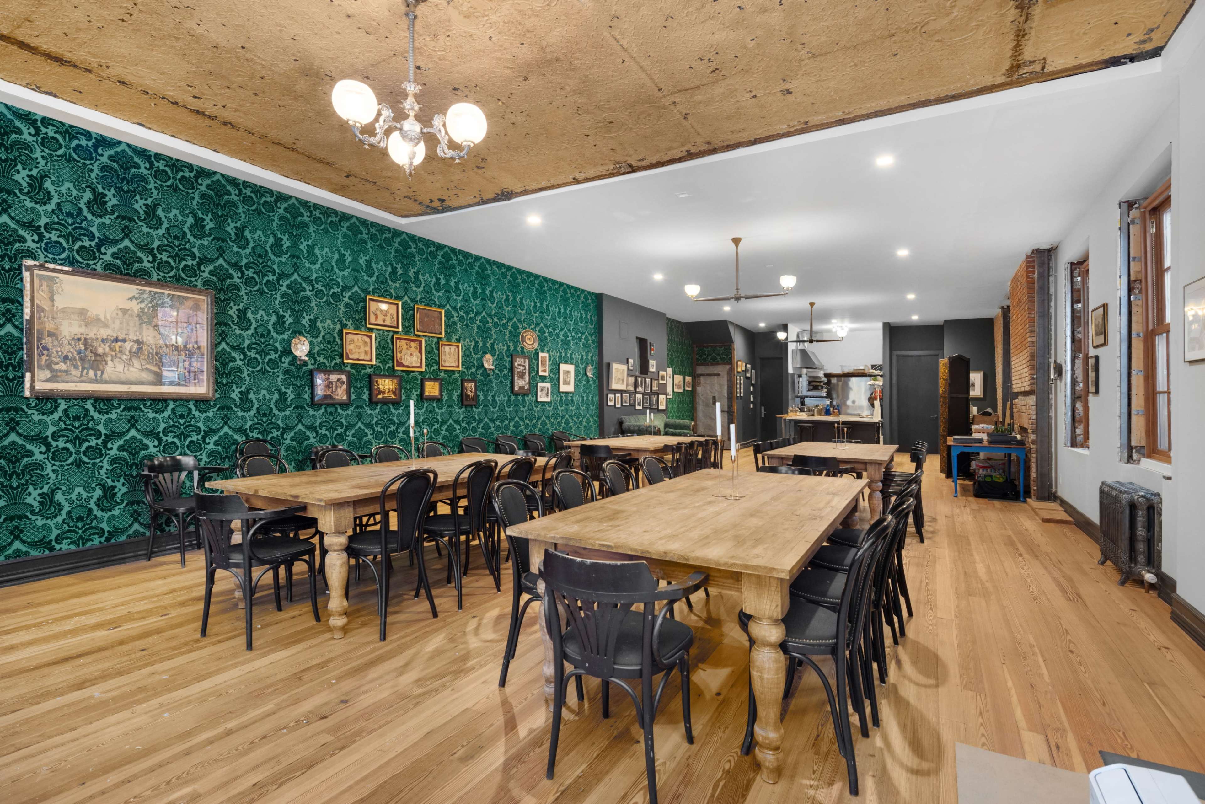 A spacious dining area with dark green patterned wallpaper, several wooden tables, and a variety of framed artworks on the walls.