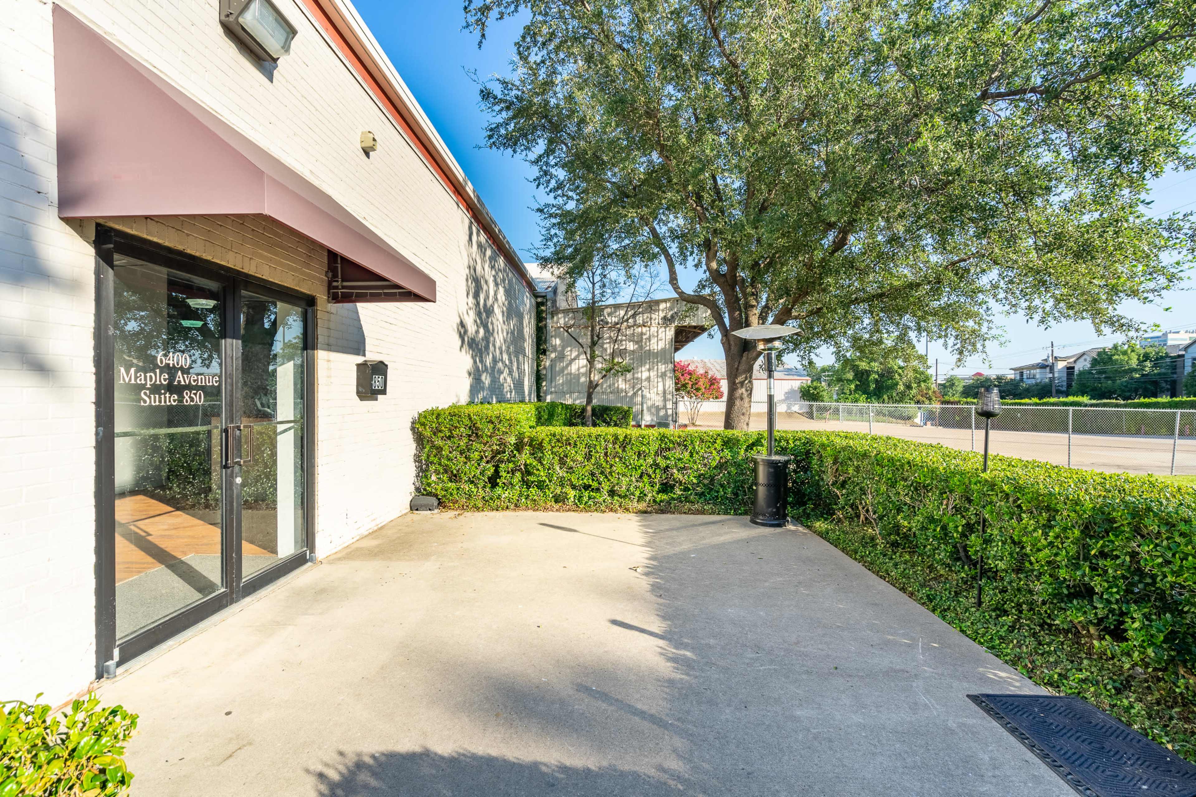 The image shows the entrance of a building with a sign indicating "490 Maple Avenue, Suite 890," surrounded by neatly trimmed hedges and a parking area.
