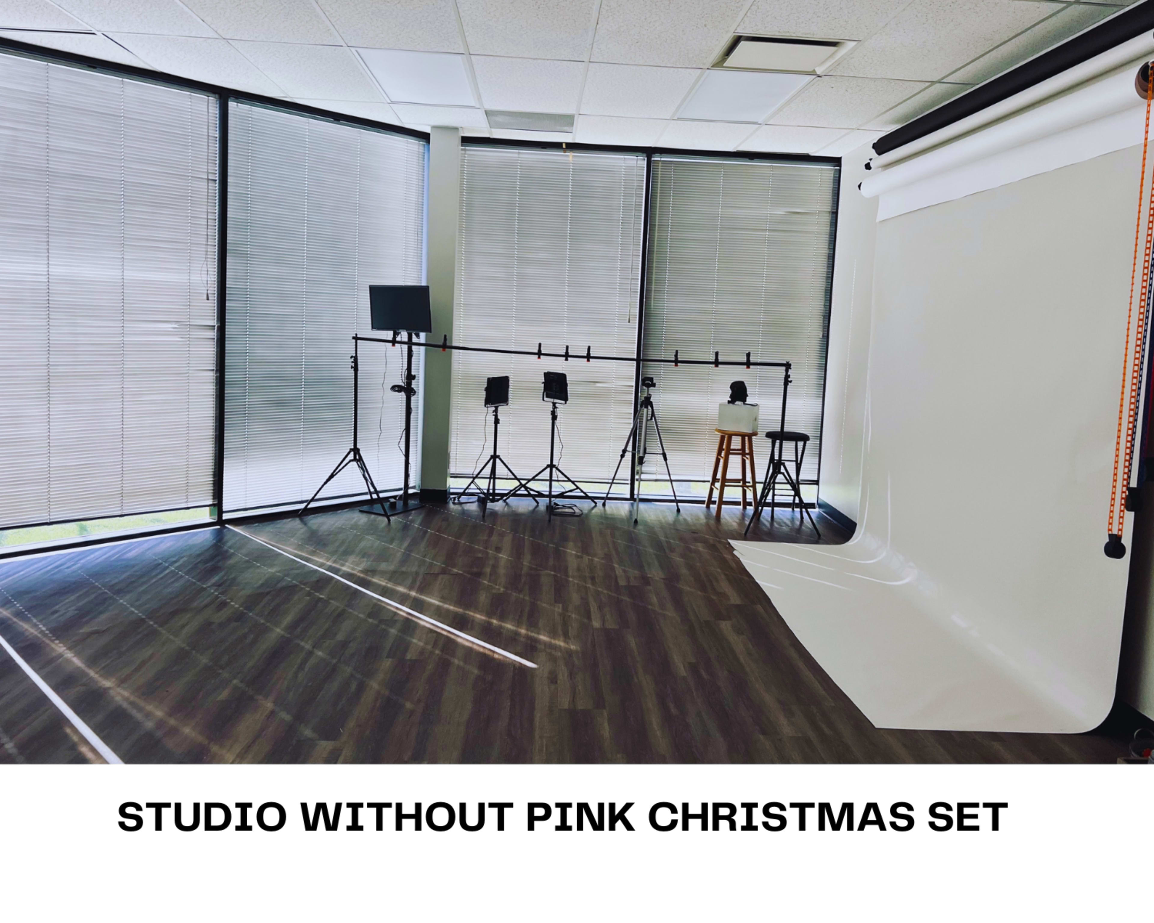 A photography studio features a plain backdrop, adjustable lighting equipment, and large windows with blinds.