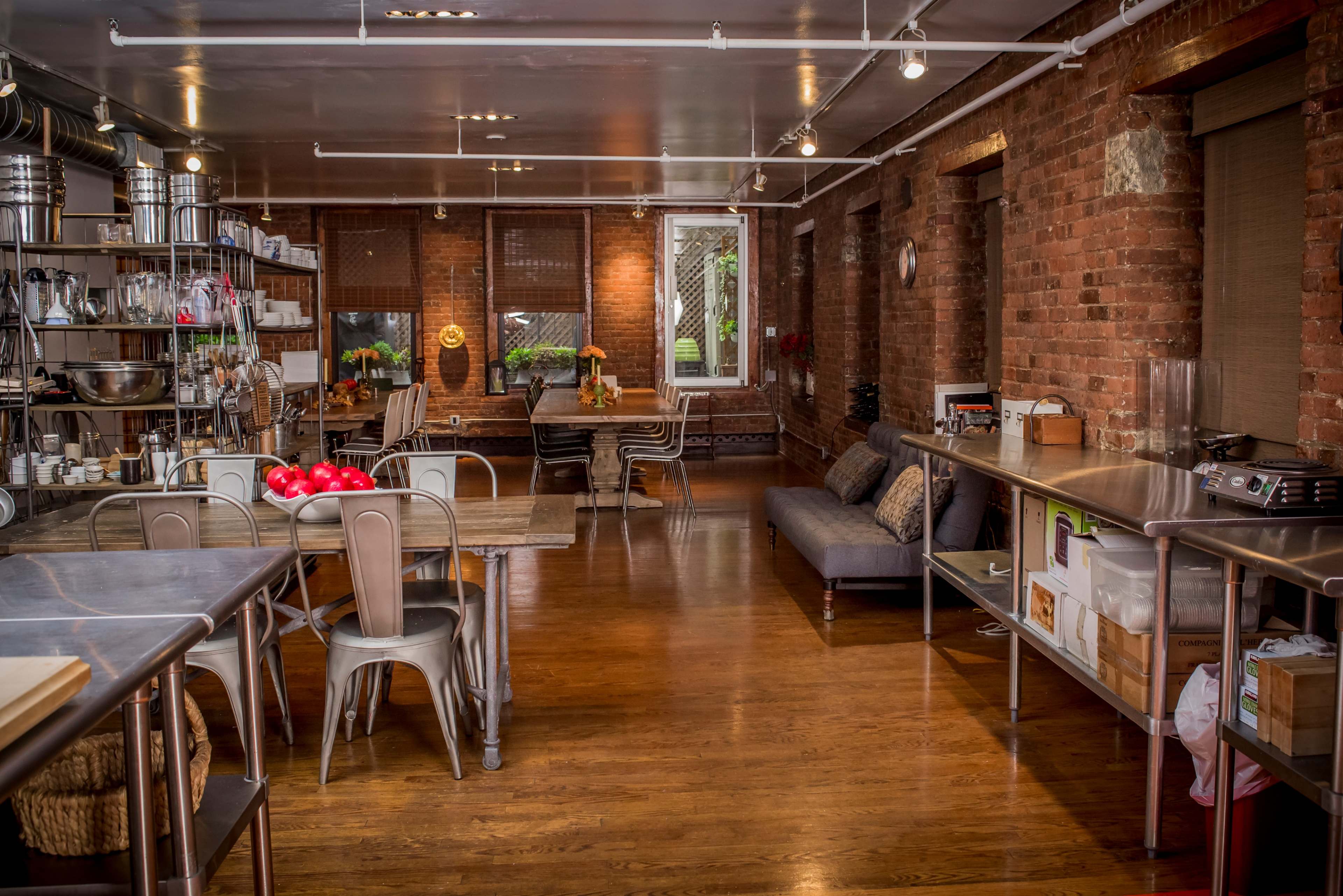 A spacious kitchen with brick walls, wooden floors, stainless steel countertops, and various kitchenware displayed on shelves.