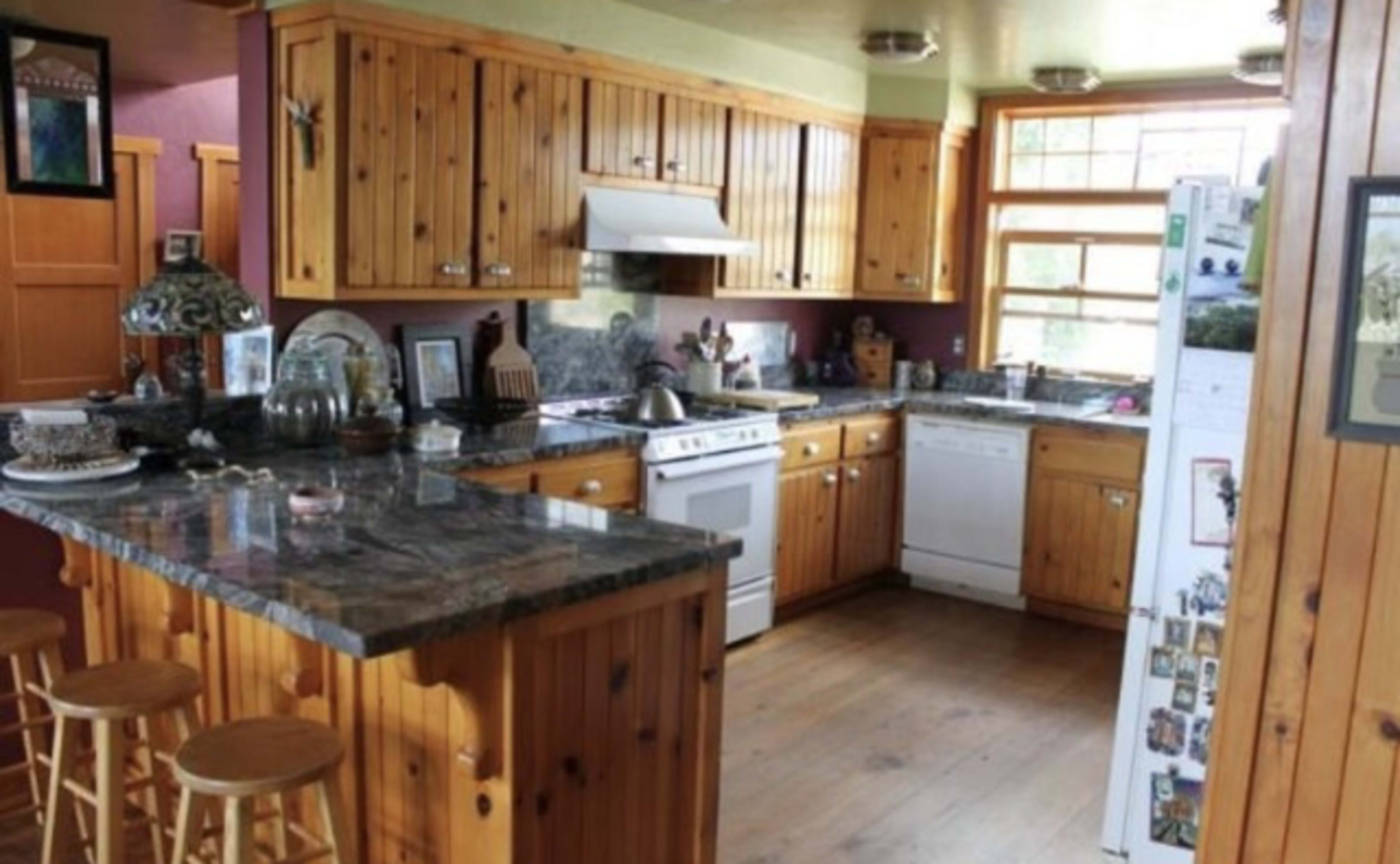 A kitchen featuring wood-paneled walls and cabinets, a central island with a granite countertop, and modern appliances.