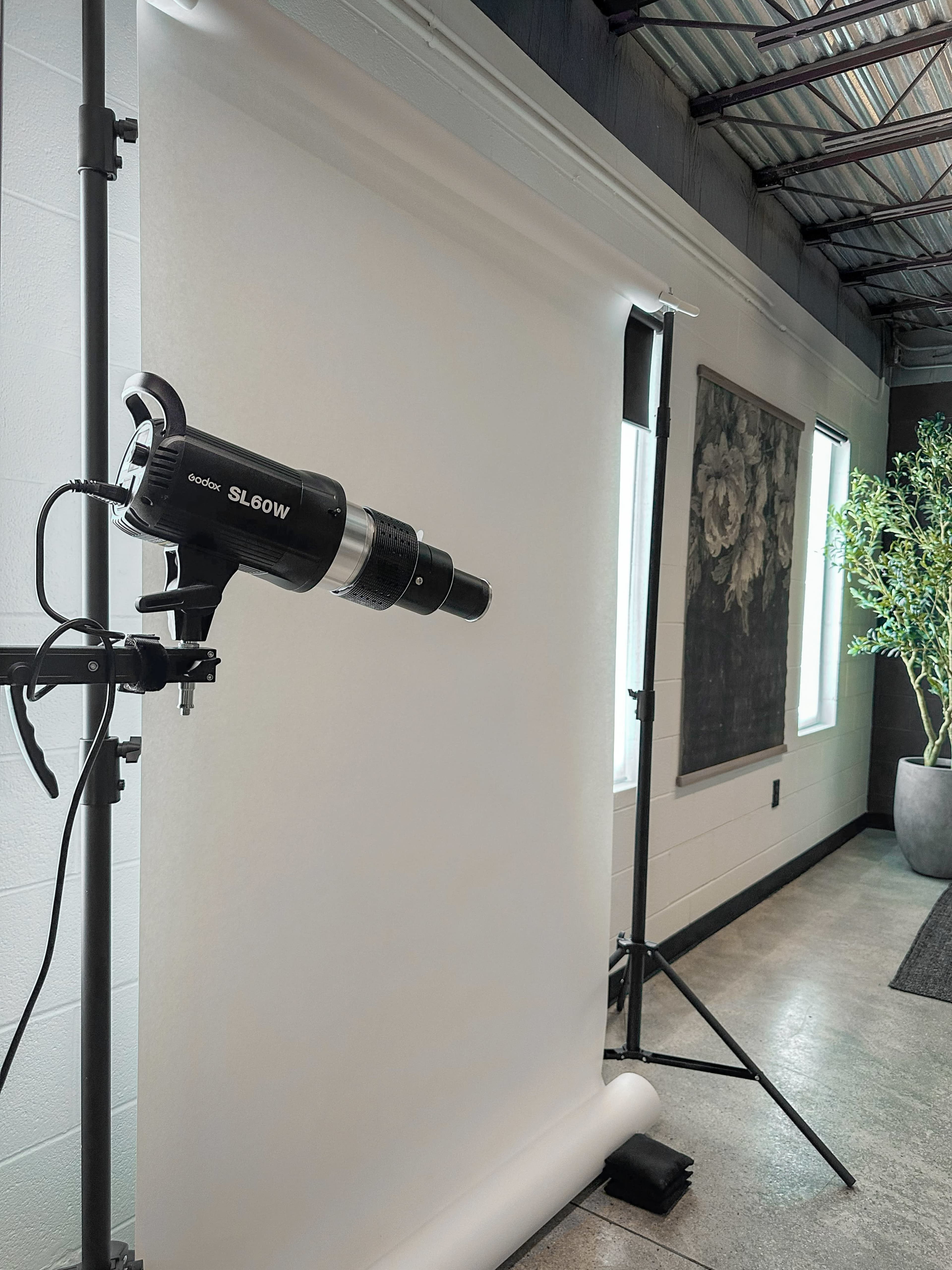 A photography studio setup features a lighting equipment mounted on a stand directed at a white backdrop.