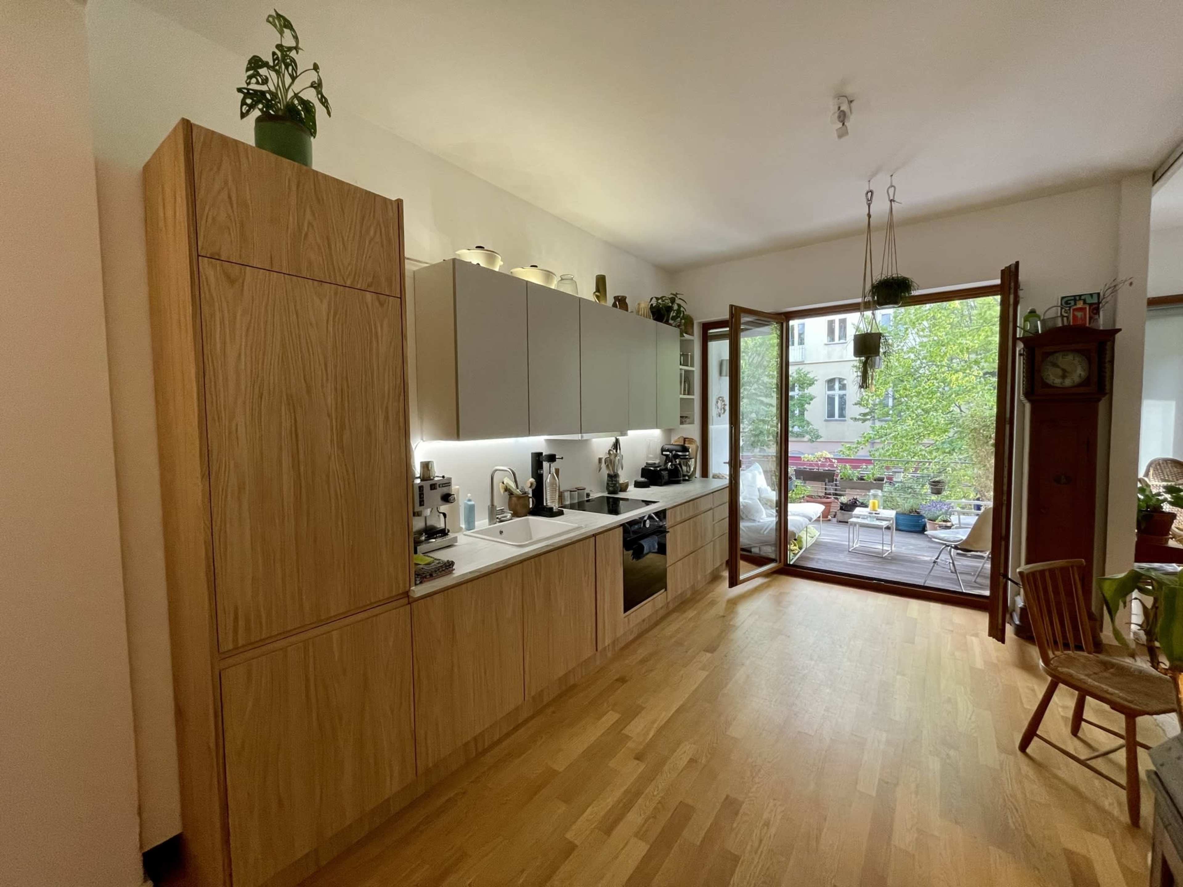 A modern kitchen features wooden cabinets, a white countertop, and an open door that leads to a patio with greenery.