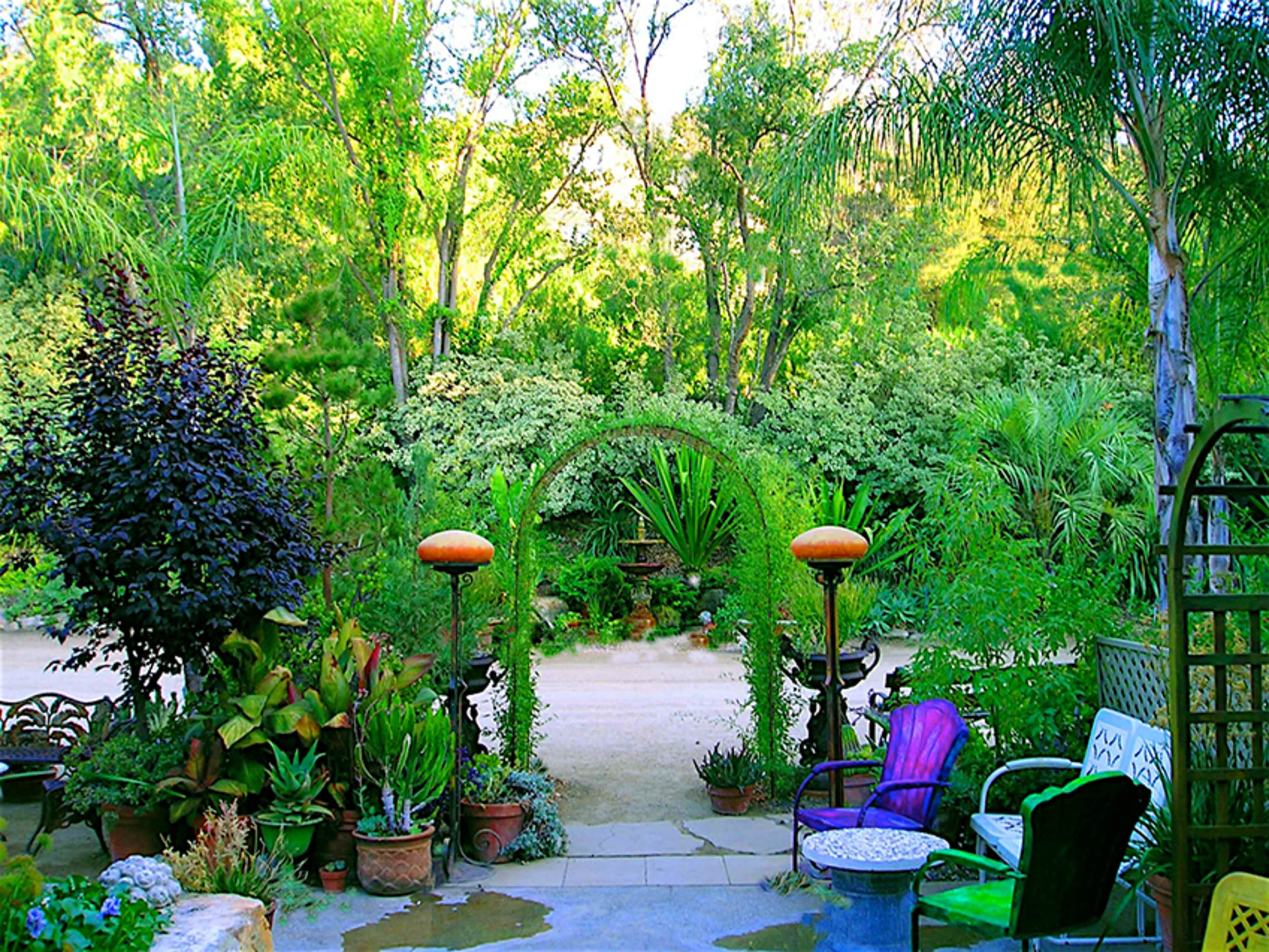 A garden pathway features an archway covered in greenery, surrounded by various plants and seating areas.