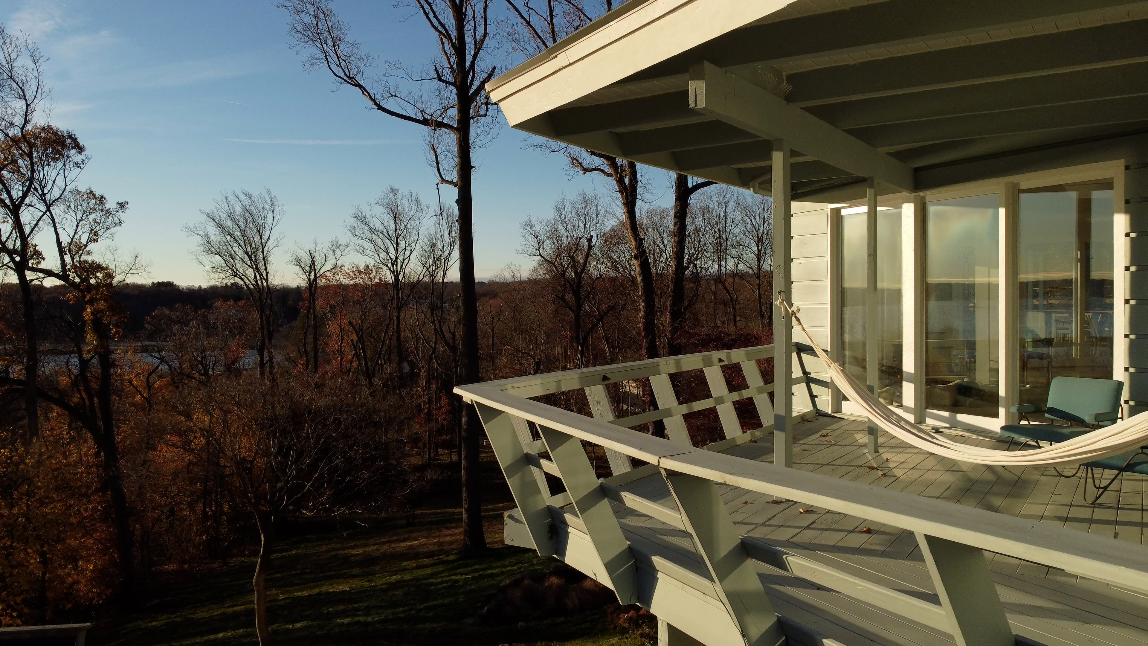 A house with a balcony overlooks a wooded area and a body of water in the distance.