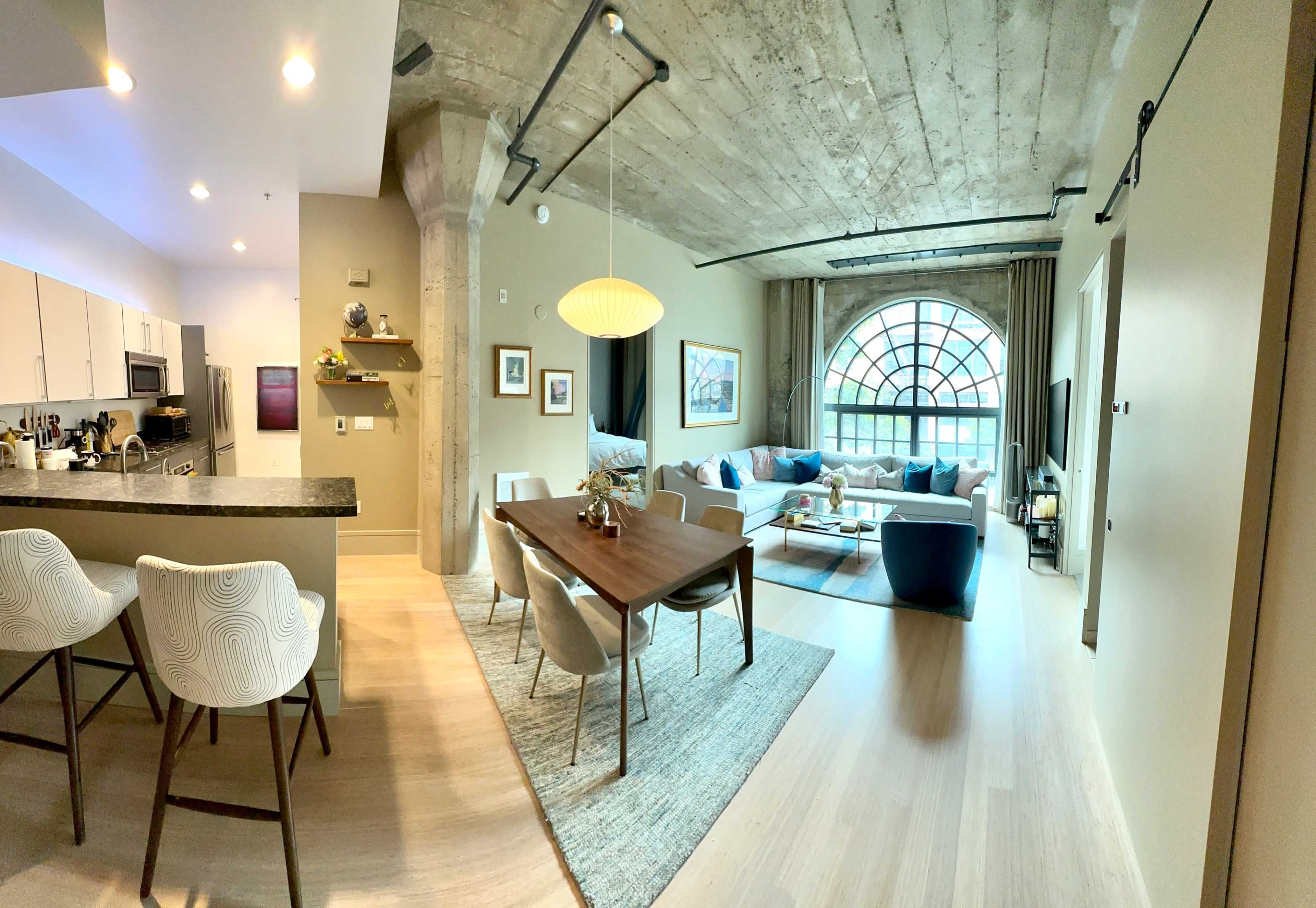 A modern open-concept living space featuring a kitchen, dining area, and a lounge with large windows.