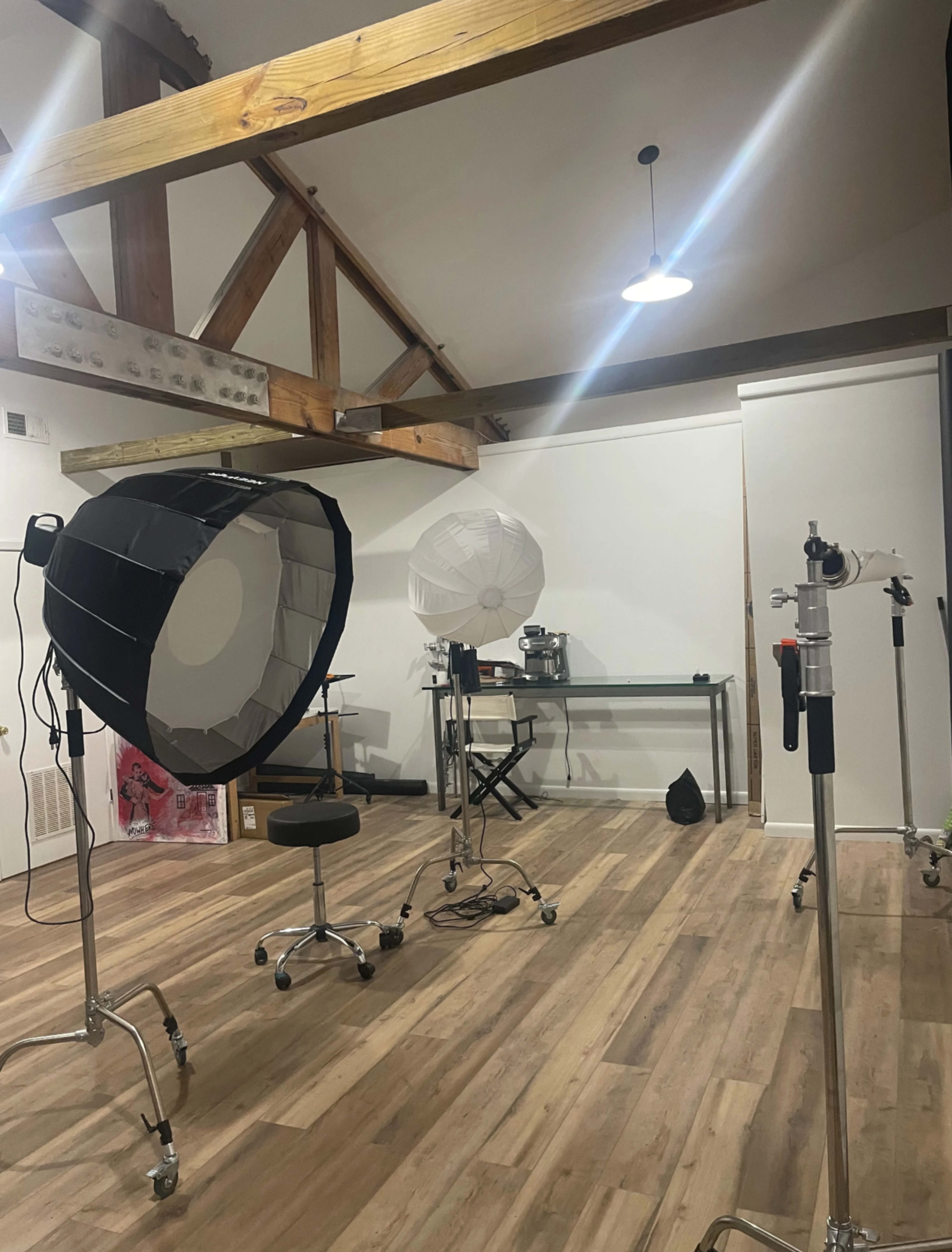A photography studio features softbox lights and a backdrop stand in a room with wooden beams and a wooden floor.