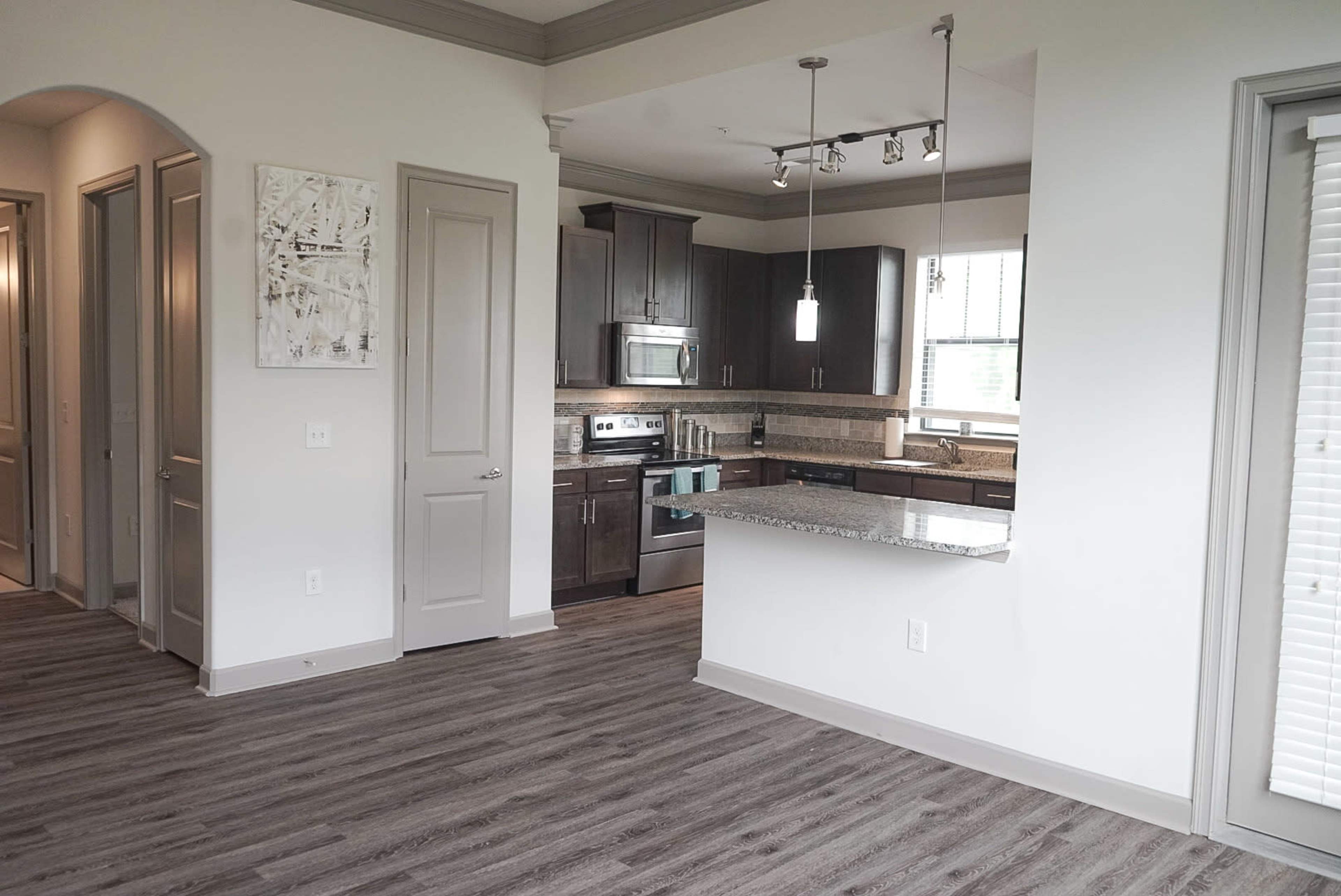 A modern open-concept kitchen and living area with granite countertops, stainless steel appliances, and light-colored cabinets.