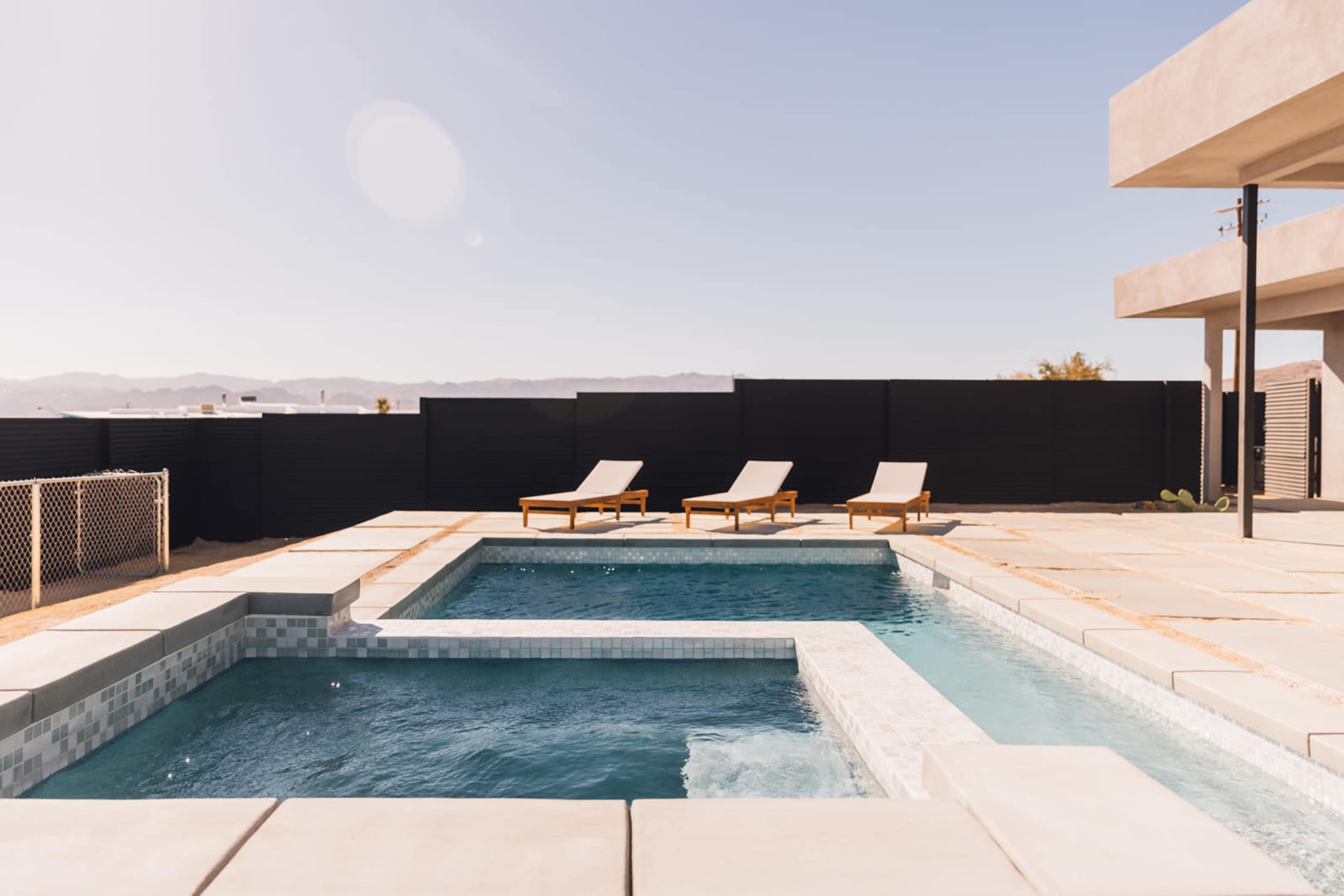 A modern outdoor pool area with two swimming pools and three lounge chairs set against a clear sky and distant mountains.