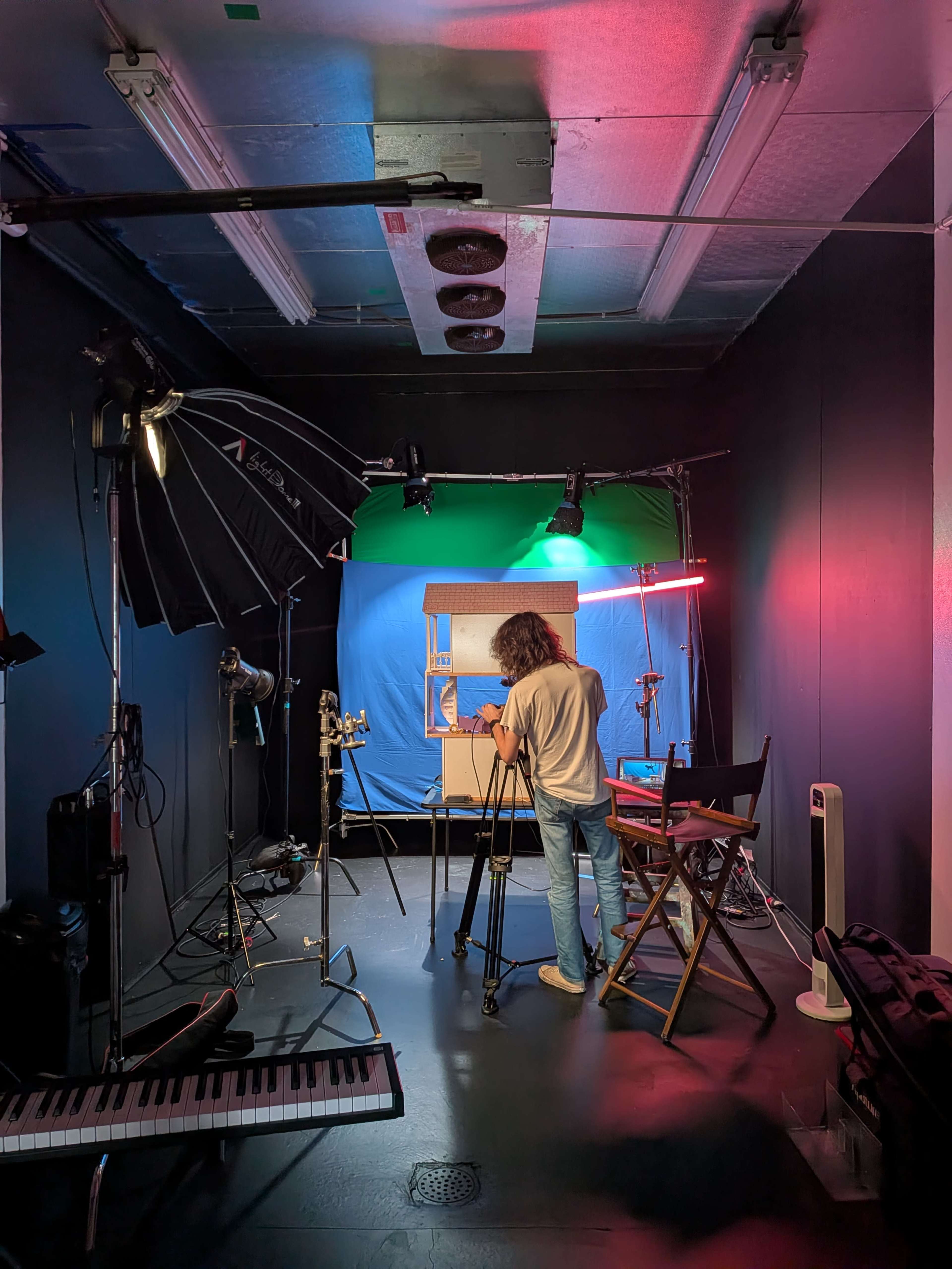 A person sets up a camera on a tripod in a studio with blue and green backdrop lighting.