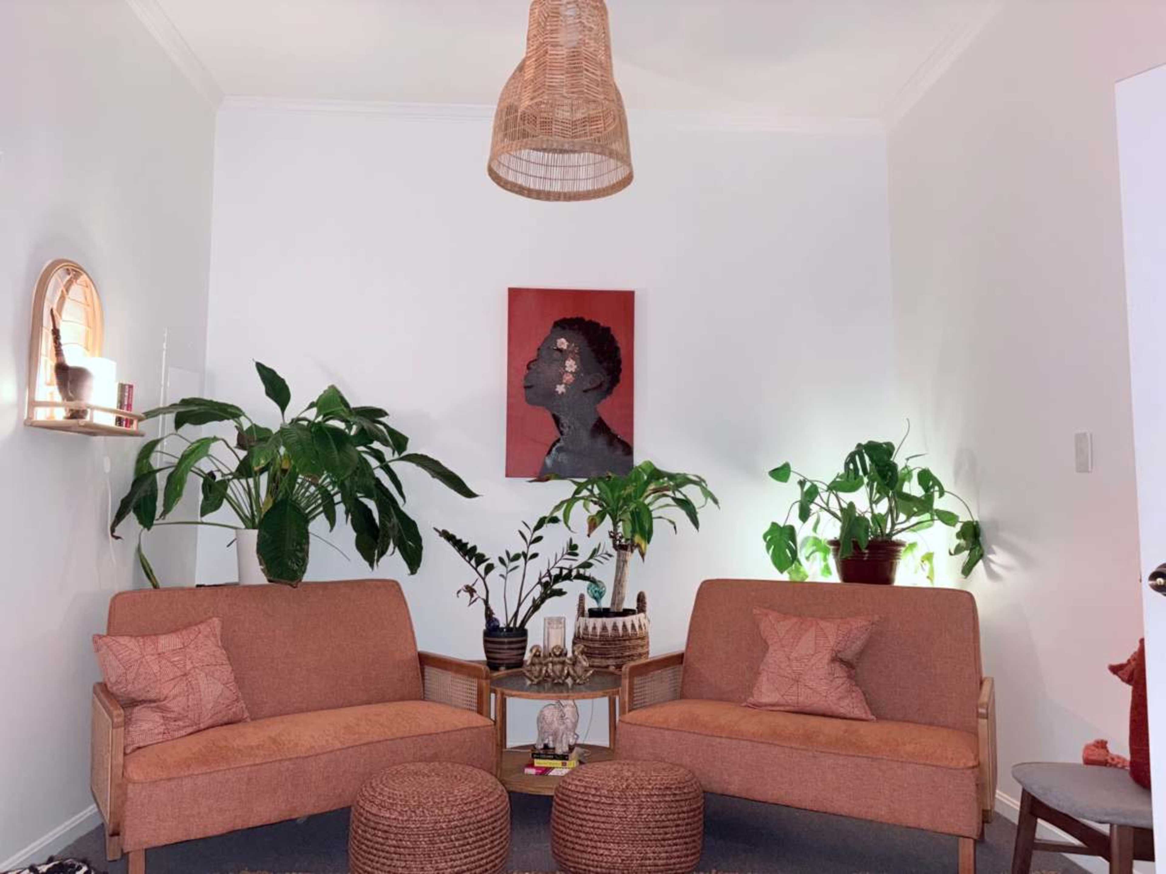 The scene shows a cozy living room with two orange sofas, a piece of artwork on the wall, and several potted plants.