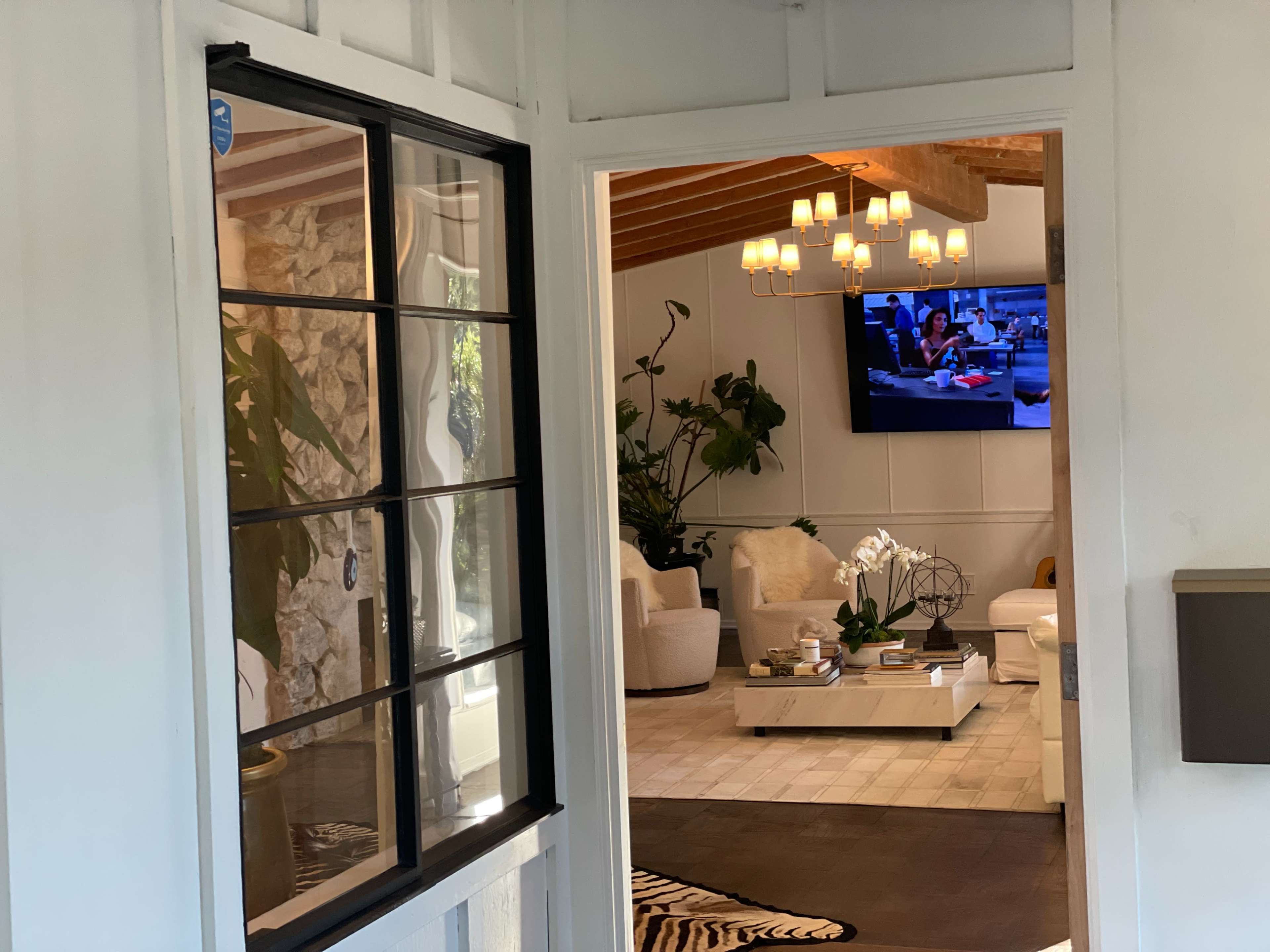 A doorway leads into a spacious indoor living area with a television, white furniture, and decorative plants.