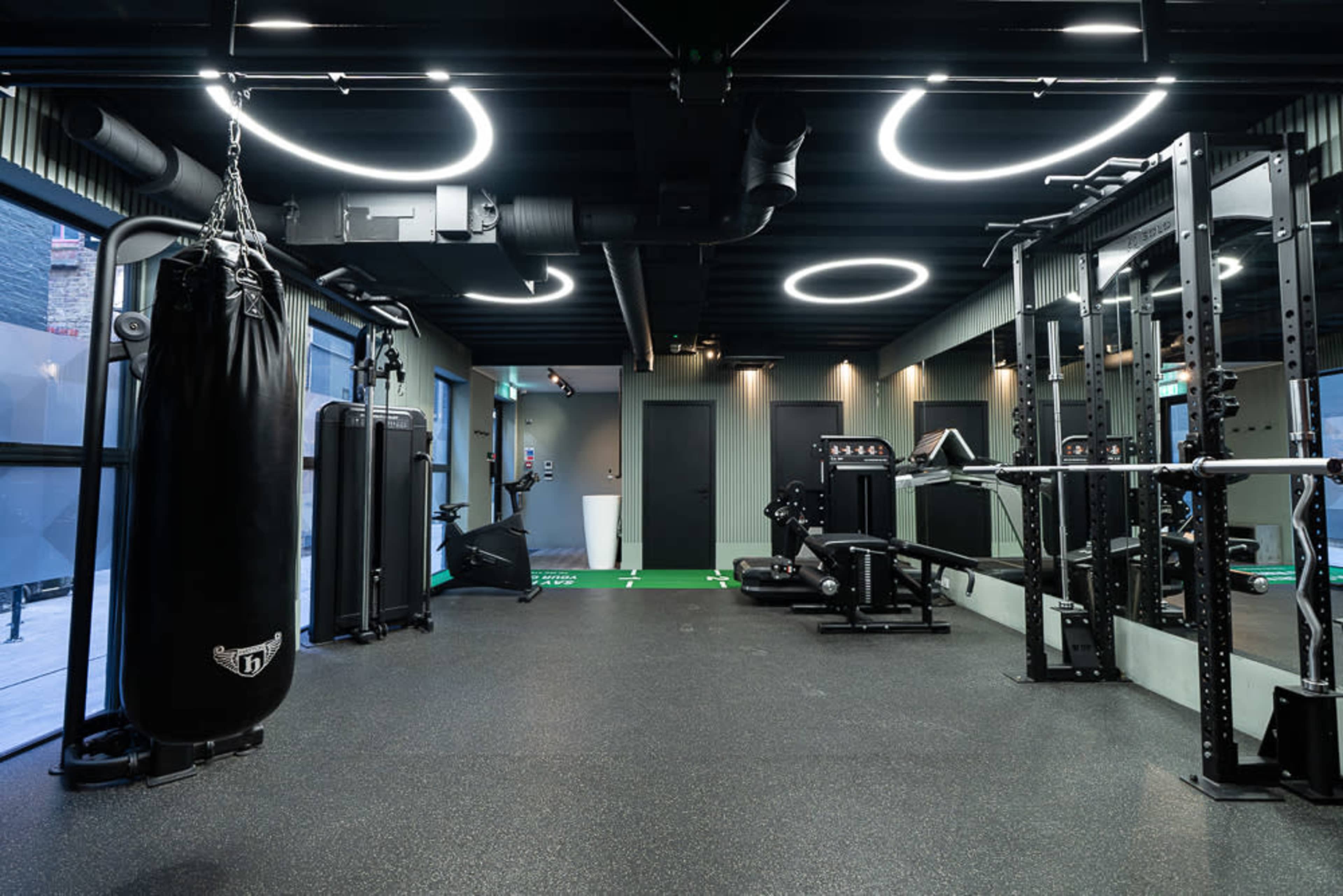 The image shows a modern gym equipped with a punching bag, strength training racks, and various fitness machines, featuring sleek black and green decor.