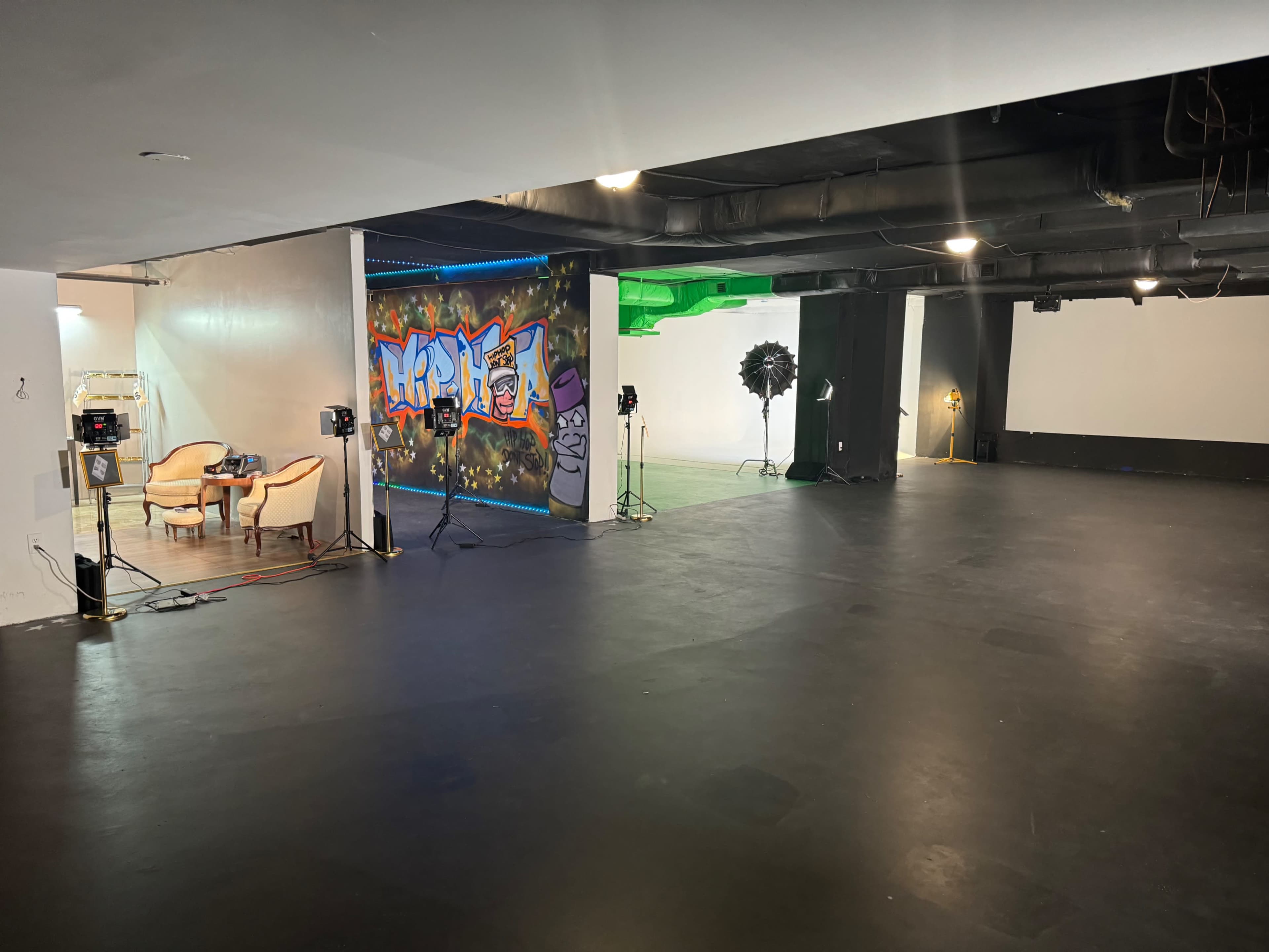 The image shows a spacious studio with a black floor, two light sources set up, colorful graffiti on the wall, and empty furniture on one side.