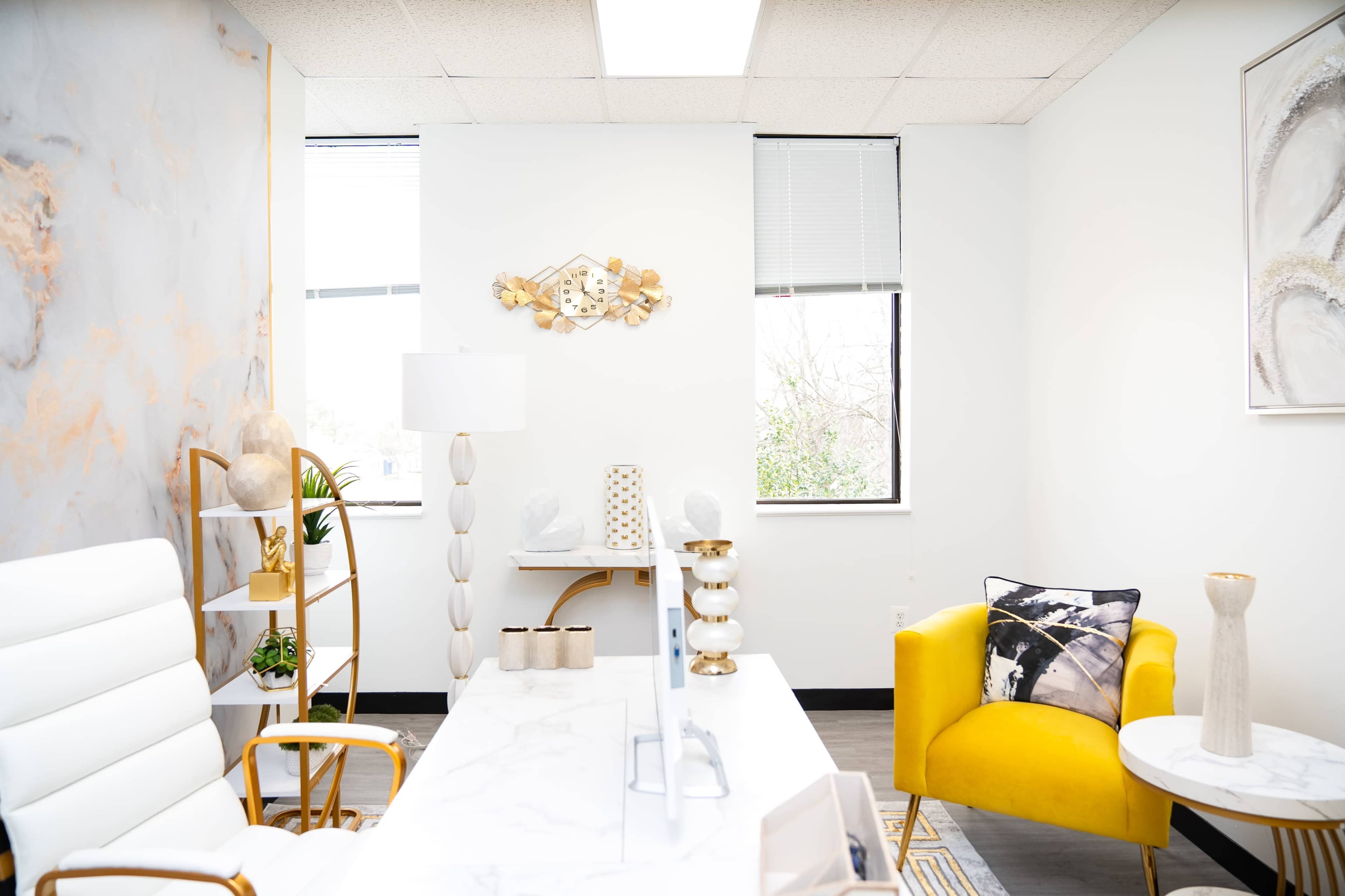 A modern office space featuring a white marble desk, a yellow accent chair, and decorative wall art.