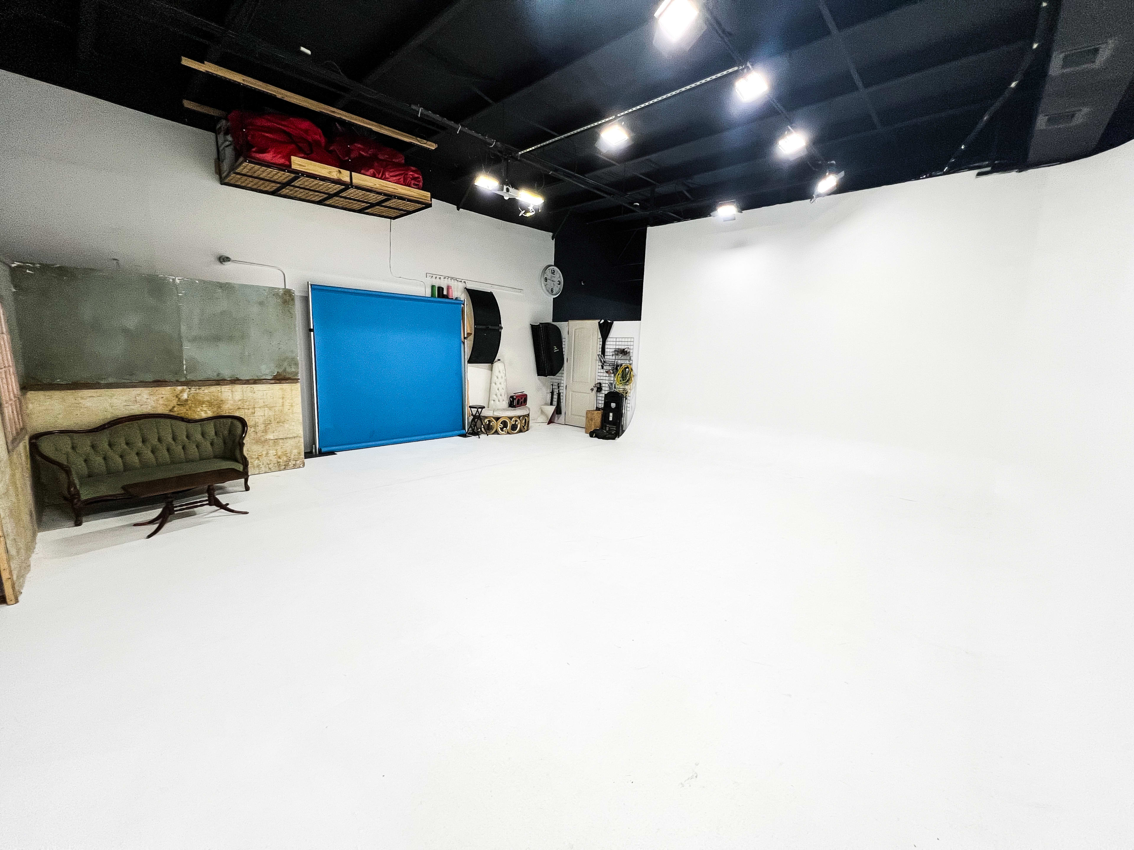 A spacious, empty studio with white walls, a blue rolling door, and a vintage green couch in one corner.
