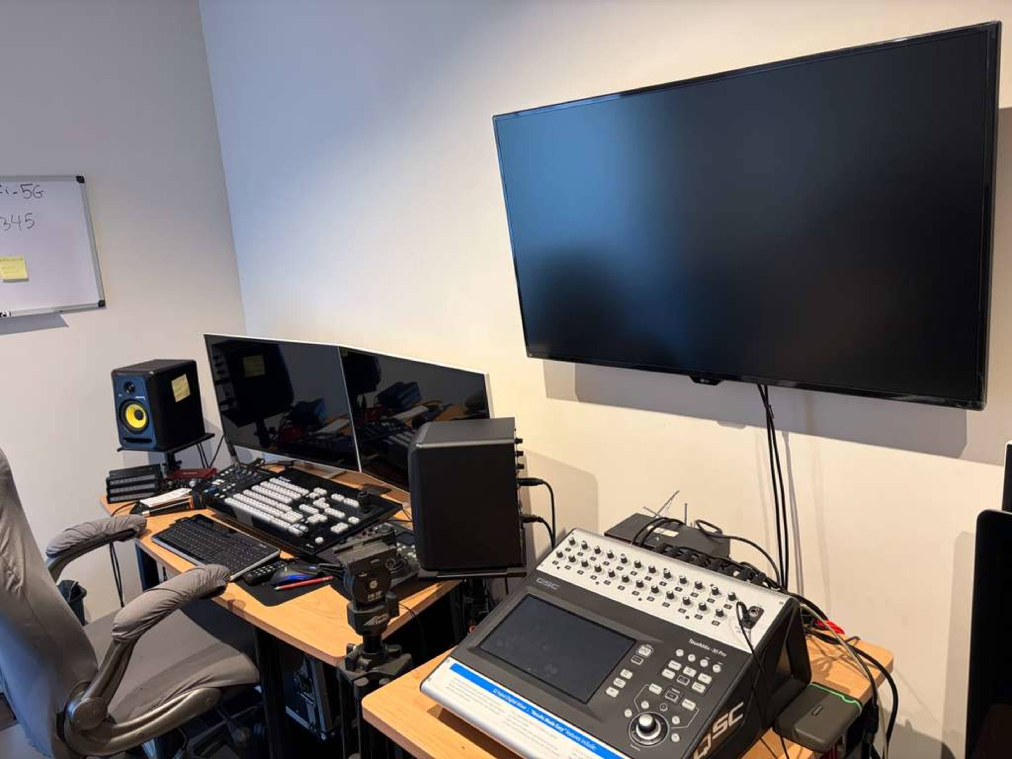 The image shows a home studio setup with two monitors, an audio interface, and a television mounted on the wall.