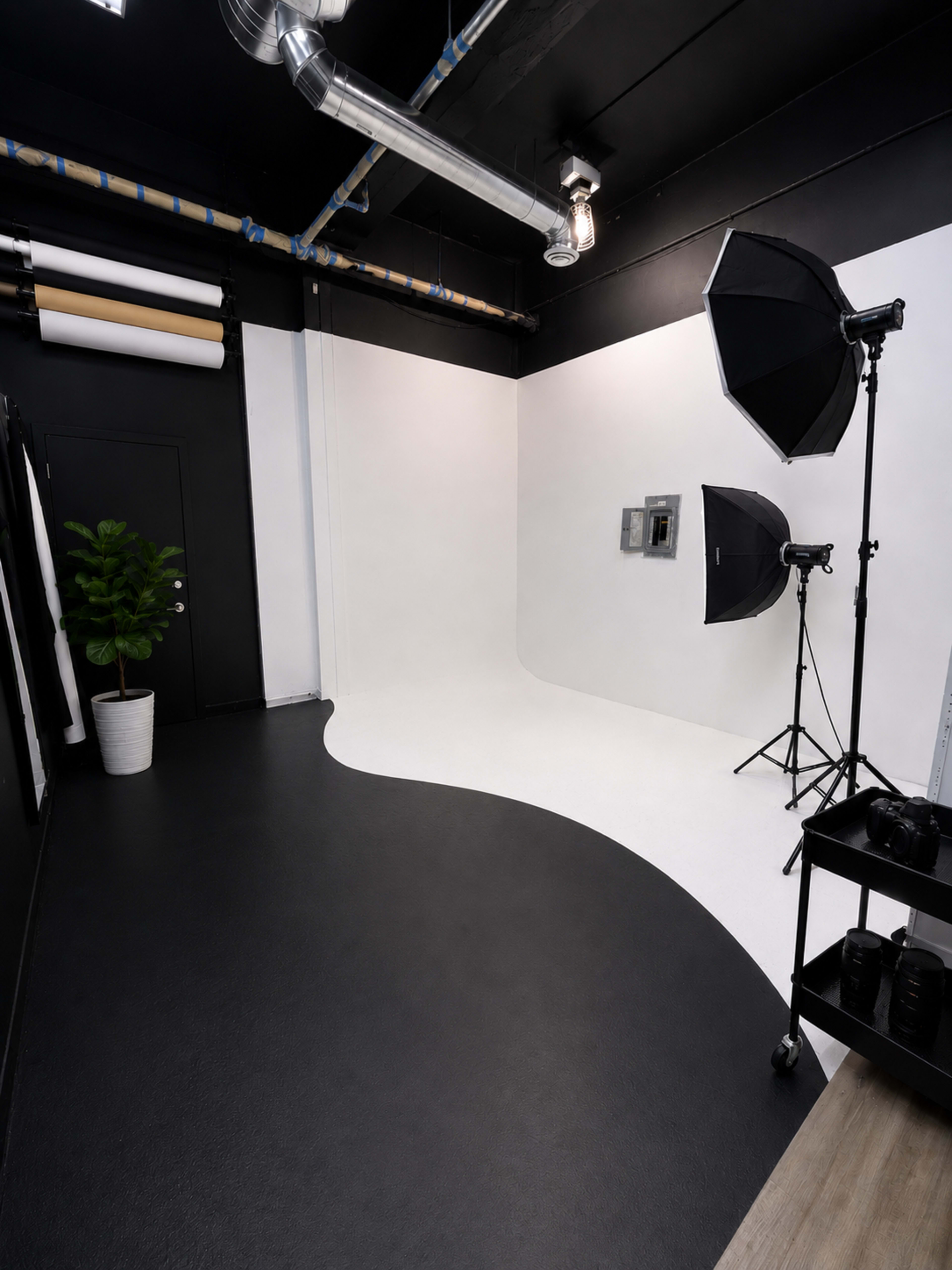 The image shows a photography studio with a curved backdrop, studio lights on stands, and a black and white floor design.