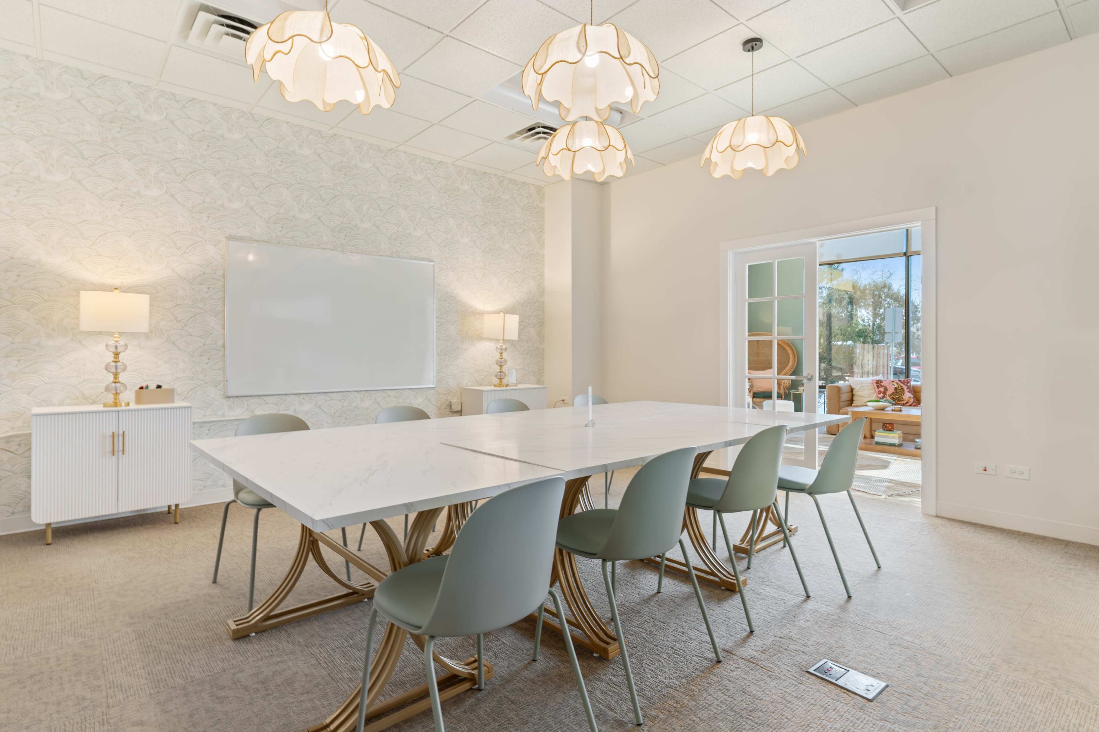A modern conference room features a large marble table surrounded by light green chairs, with decorative lamps and a whiteboard on the wall.