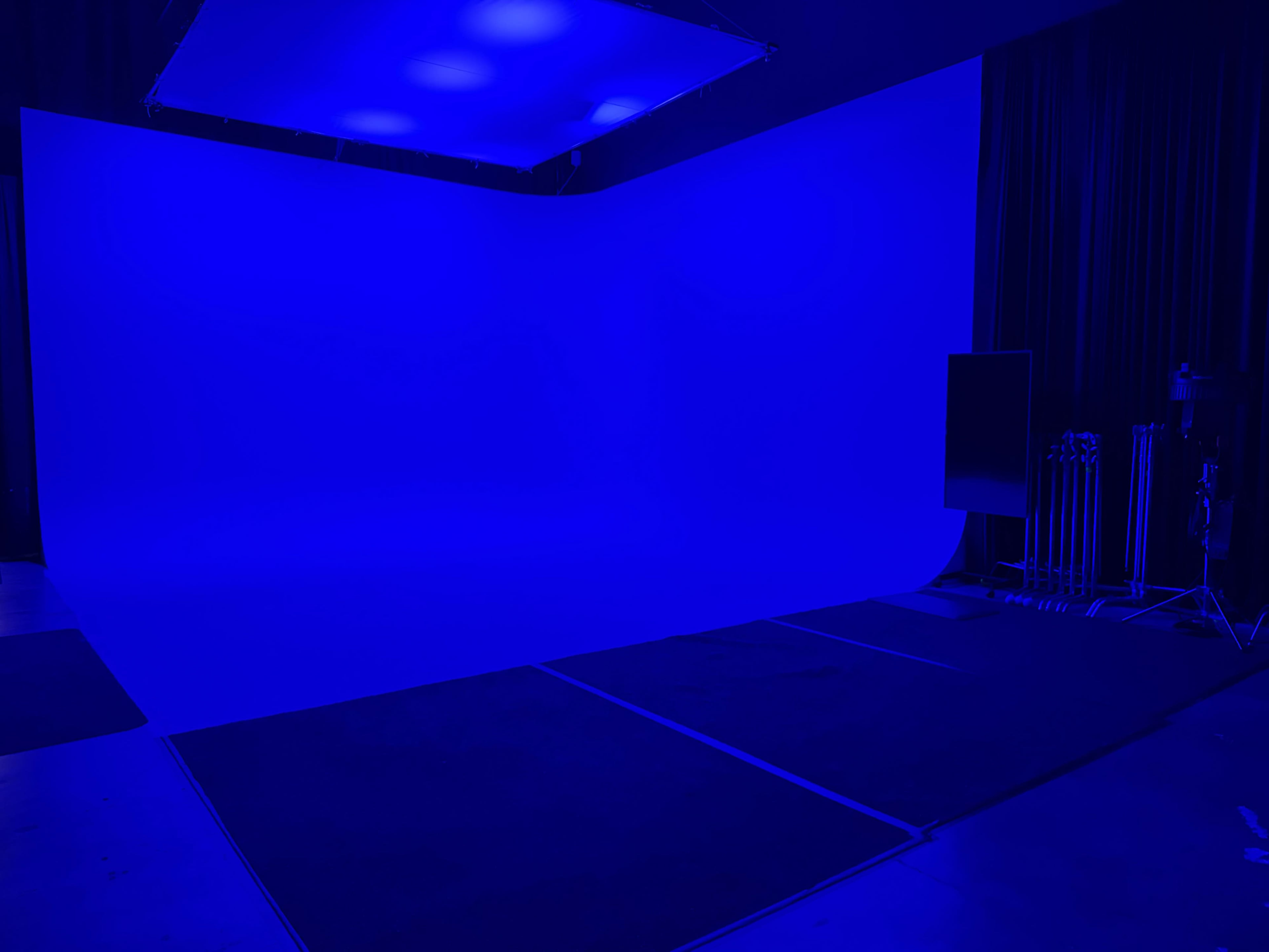 The image shows a studio space with a blue backdrop, dim lighting, and equipment set up along one side.
