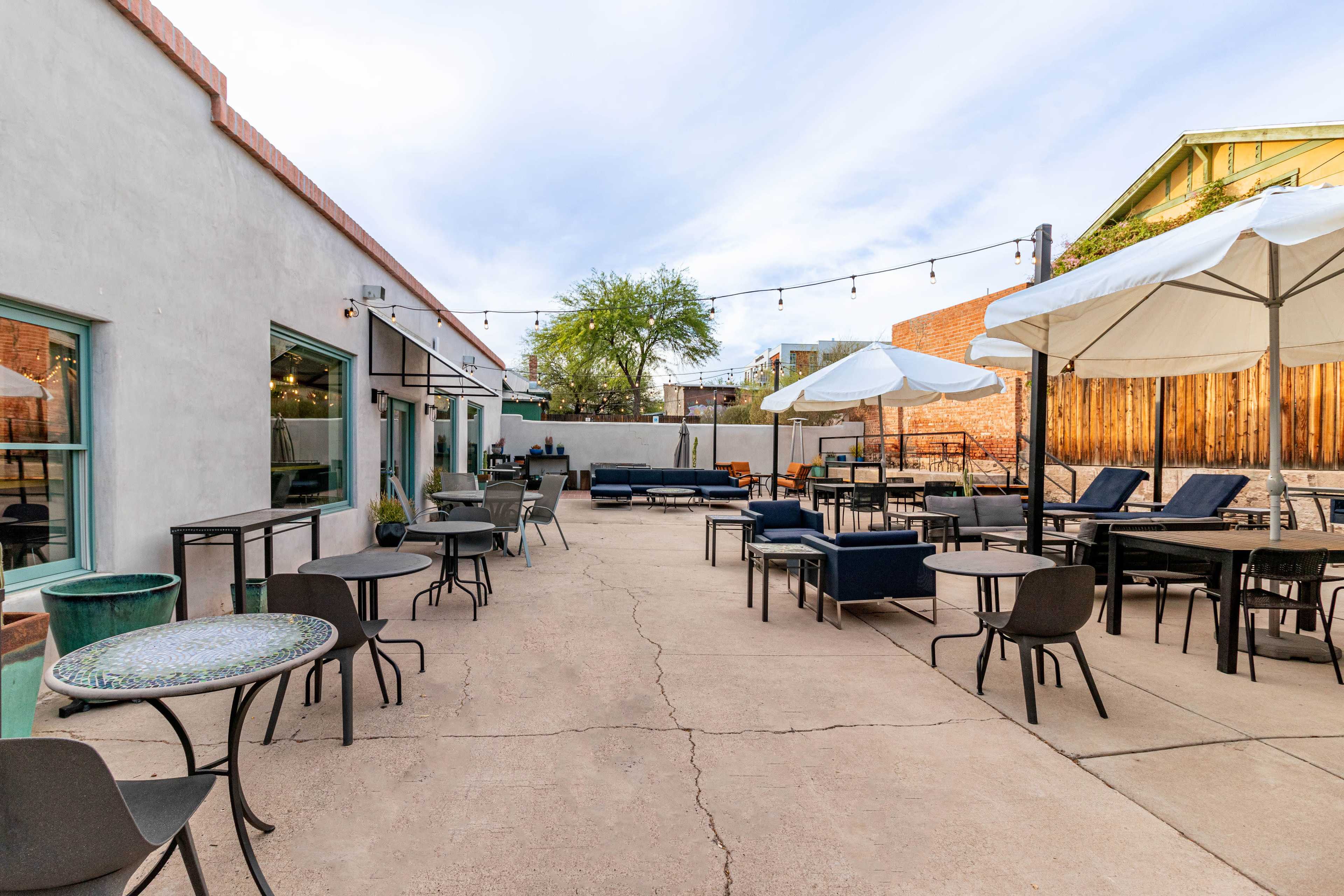 An outdoor patio area with tables, chairs, and umbrellas, surrounded by walls and buildings.