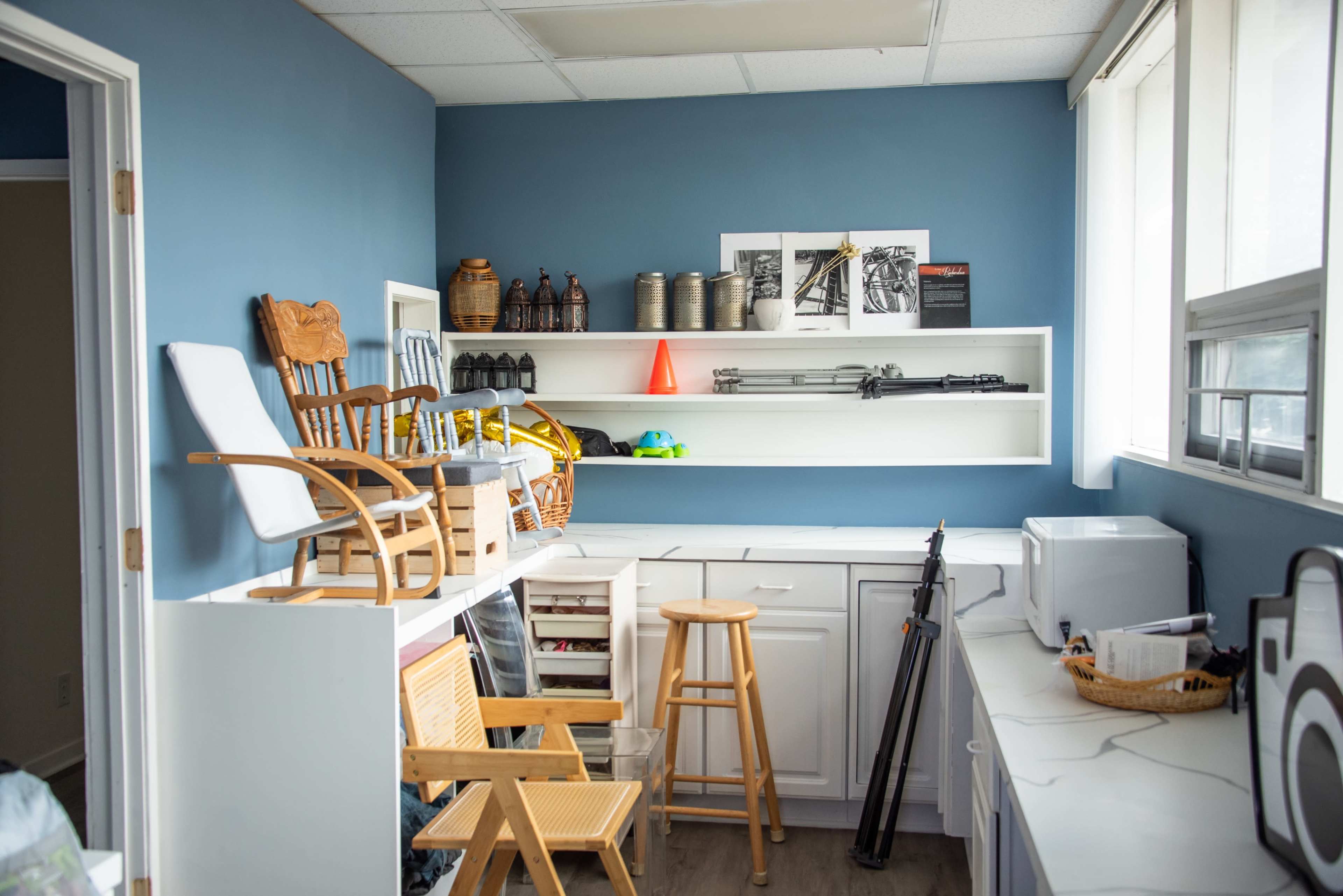 The image shows a small storage room with shelves containing various items, including chairs, baskets, and containers, against a blue wall.